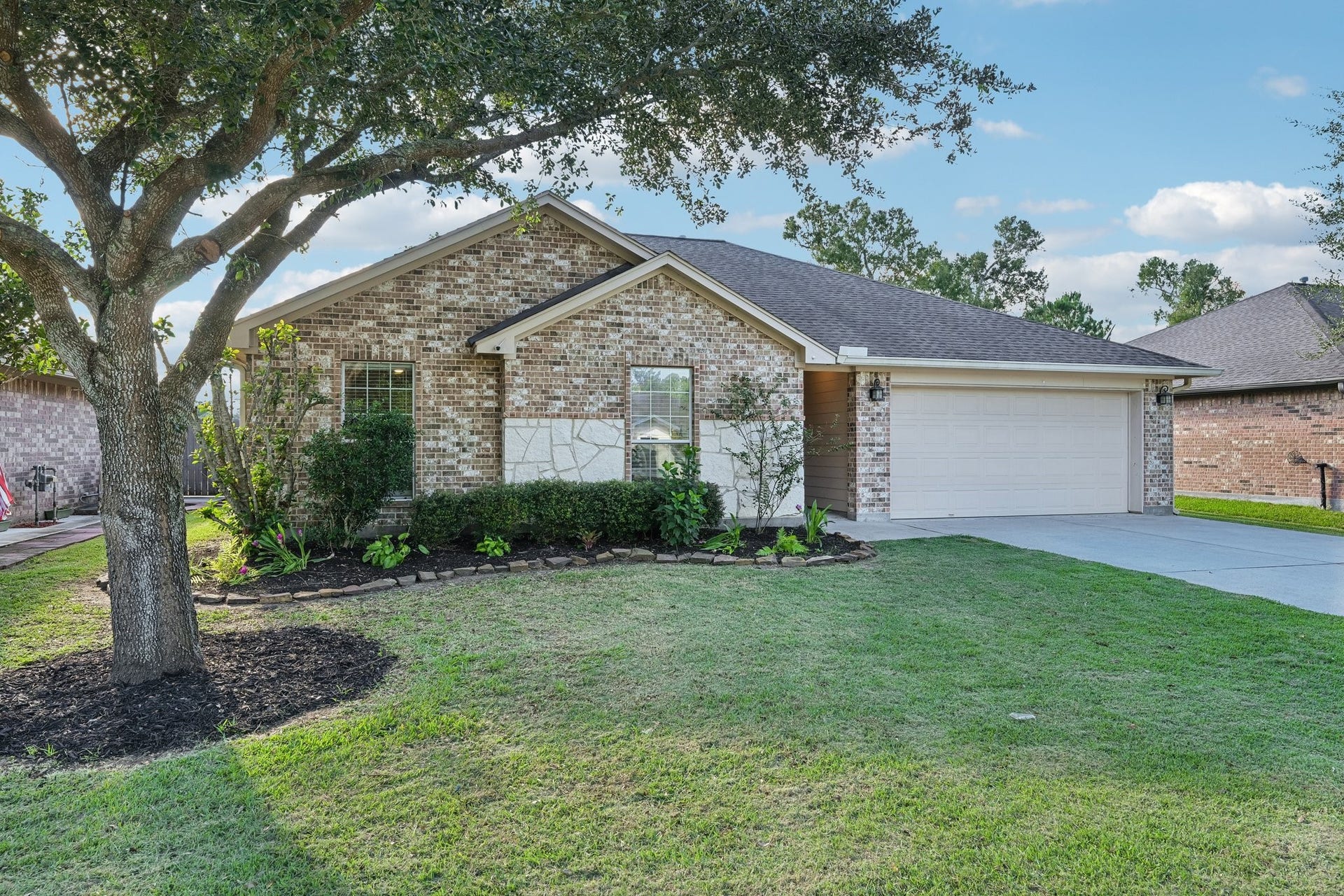 5012 Bayou Dr, Dickinson, TX 77539 Charming brick home with a beautifully manicured lawn, shaded by mature trees, and a spacious two-car garage.