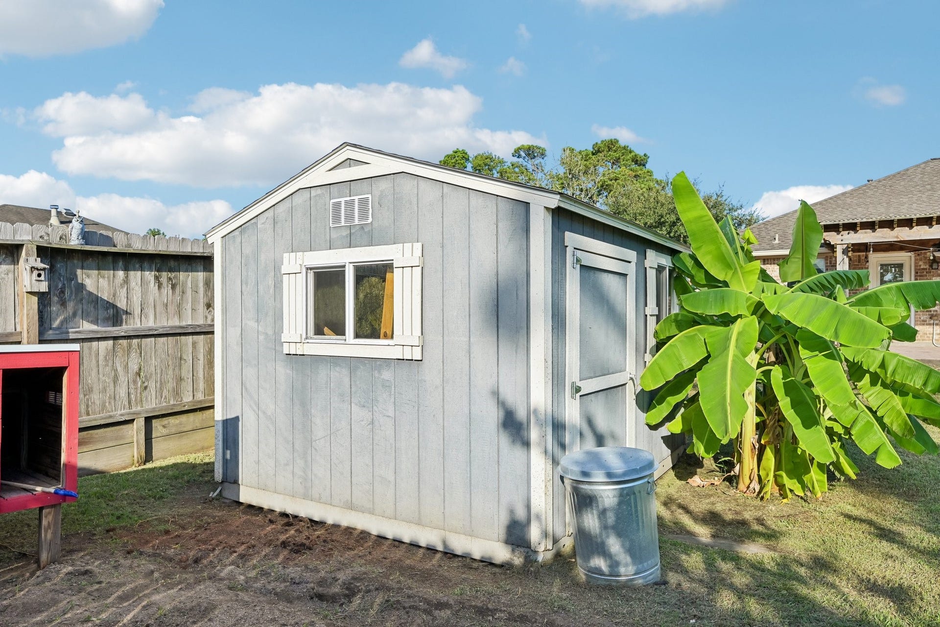 5012 Bayou Dr, Dickinson, TX 77539 Charming backyard shed with a window, nestled beside lush banana plants, offers convenient storage space in a tranquil setting.