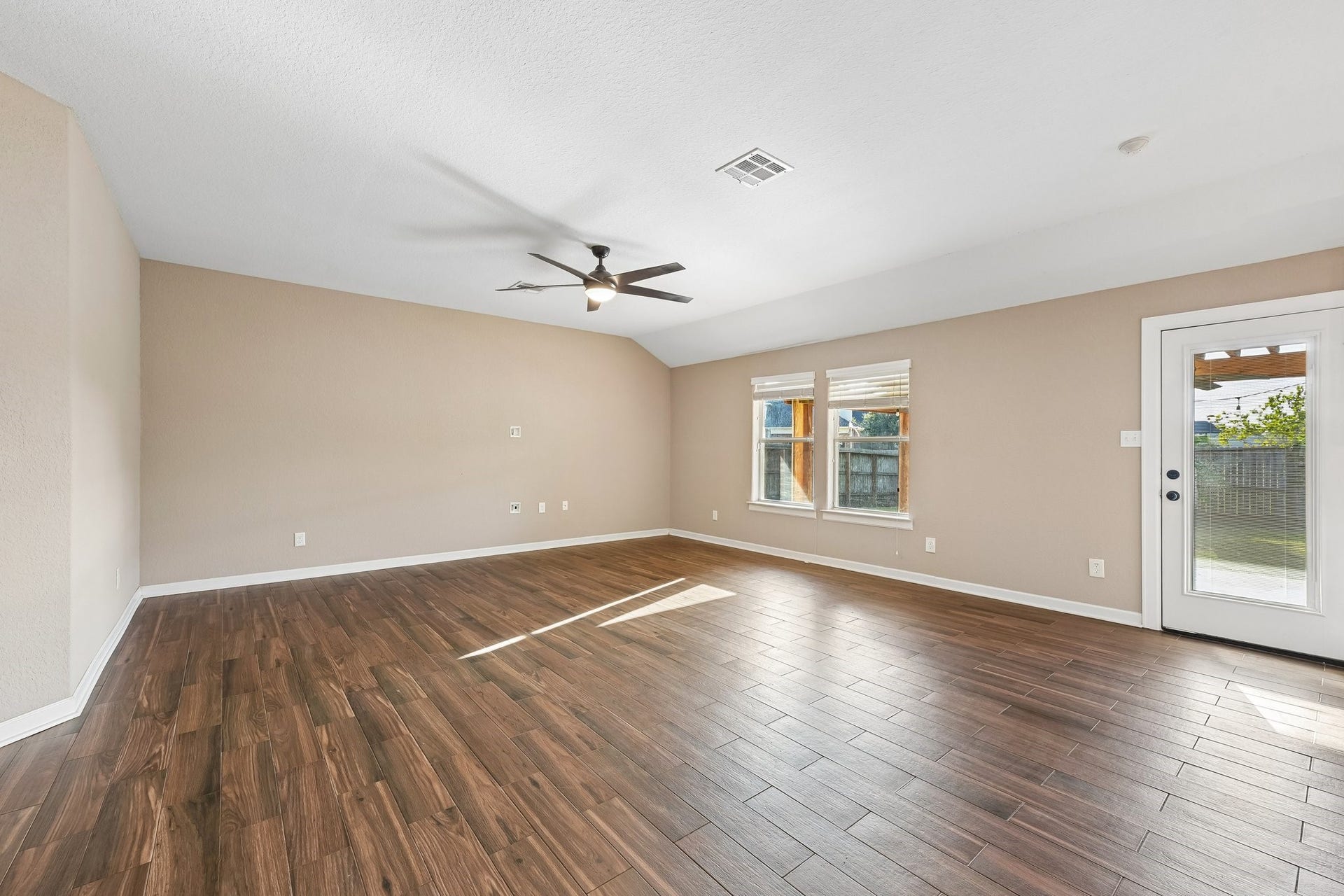 5012 Bayou Dr, Dickinson, TX 77539 Spacious living area with elegant wood flooring, abundant natural light, and a stylish ceiling fan, leading to a backyard through glass doors.