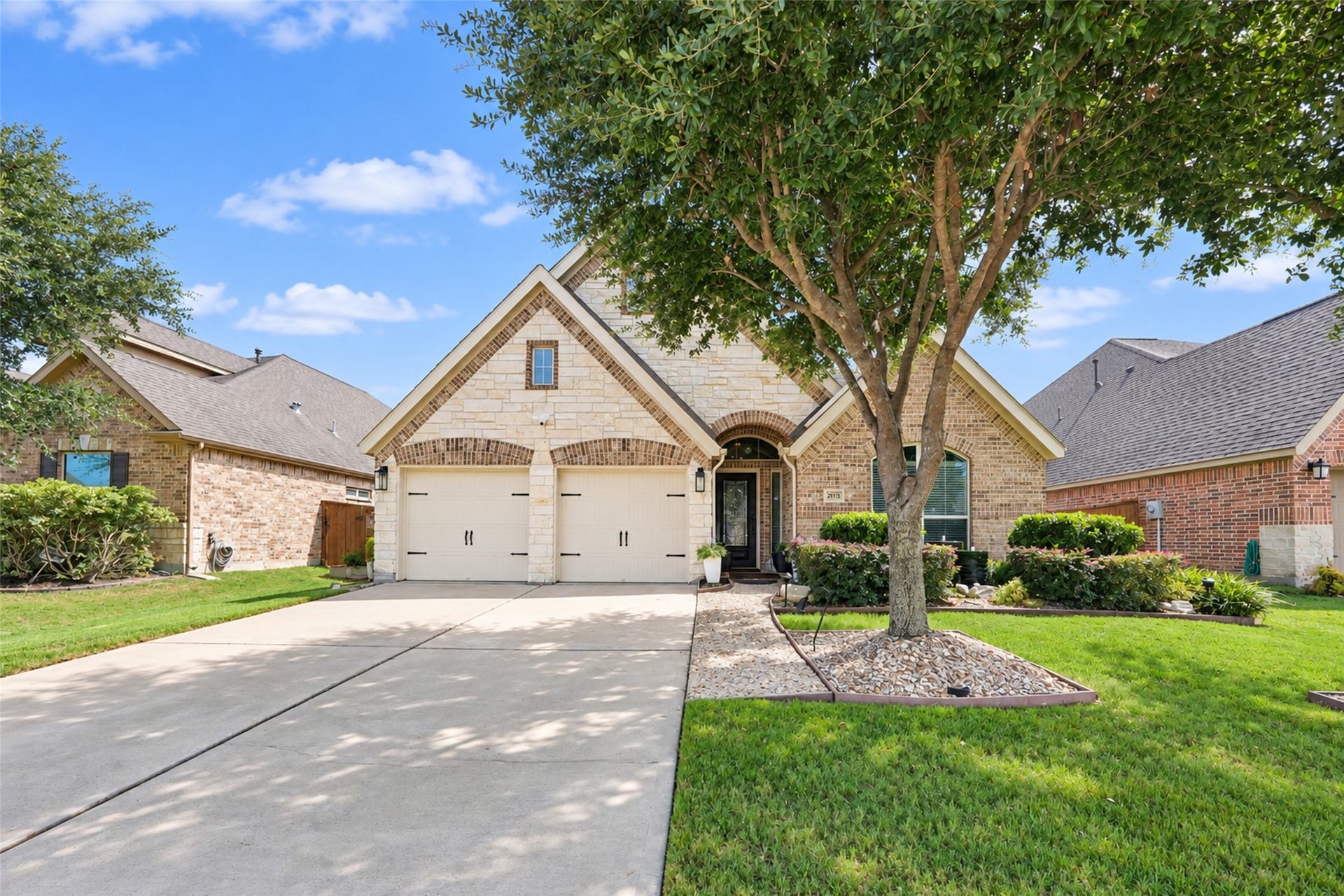 23915 Via Viale Drive, Richmond, TX 77406 Charming brick and stone exterior home with a welcoming arched entryway, lush landscaping, and a spacious two-car garage, all nestled in a serene neighborhood setting.