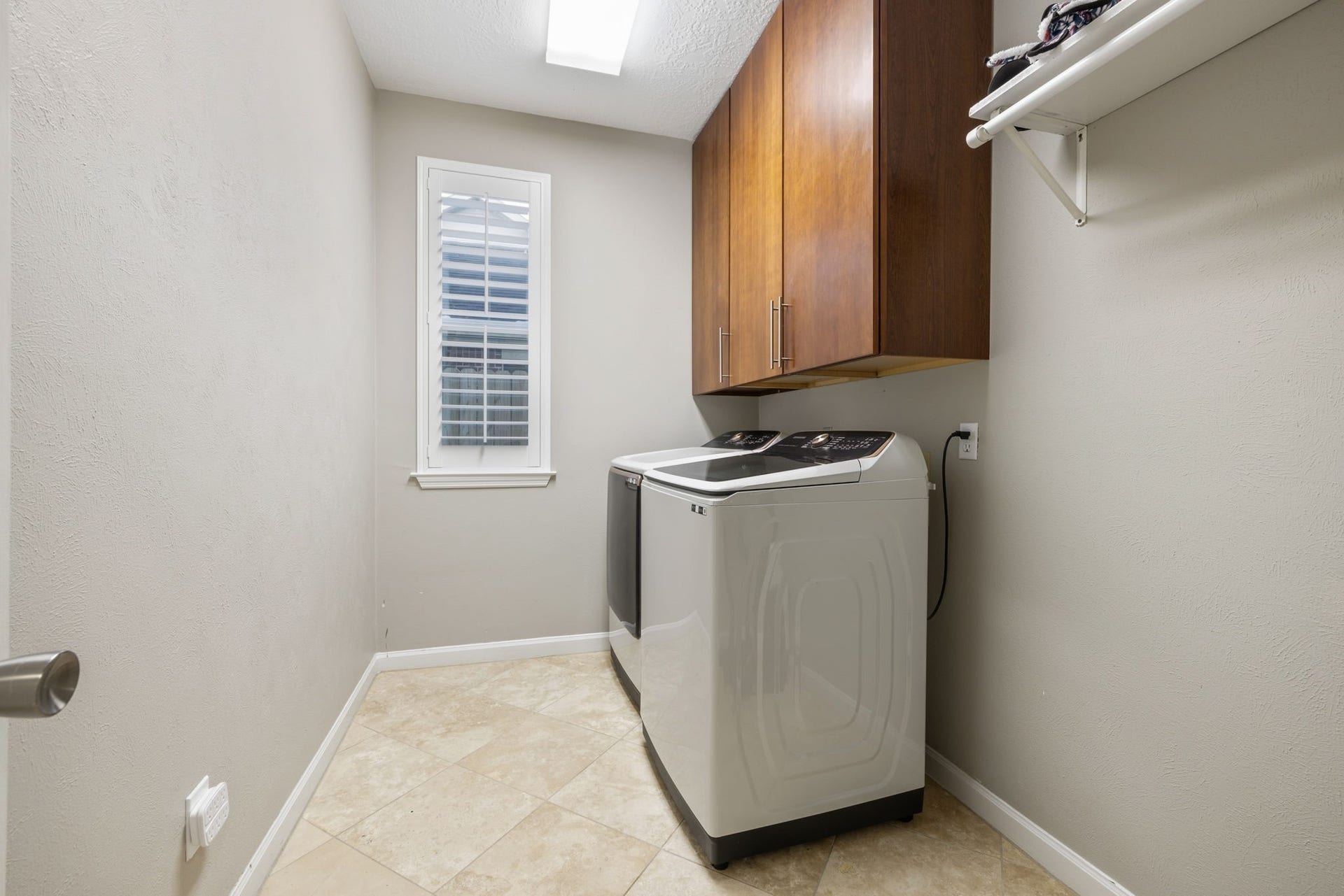 236 Sunset Ridge Drive, League City, TX 77573 Modern laundry room featuring a sleek washer and dryer, ample cabinet storage, and a bright window with shutters.