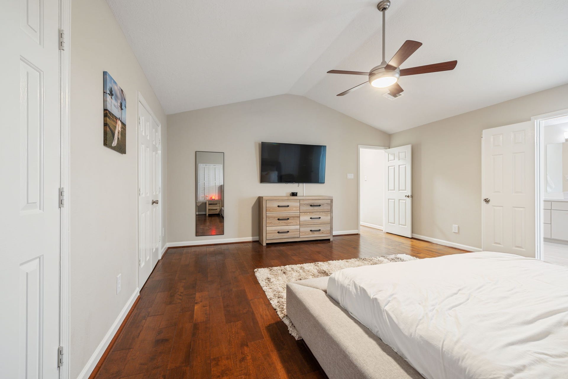 236 Sunset Ridge Drive, League City, TX 77573 Spacious bedroom featuring hardwood floors, a modern ceiling fan, and ample natural light, complemented by a sleek dresser and wall-mounted TV.