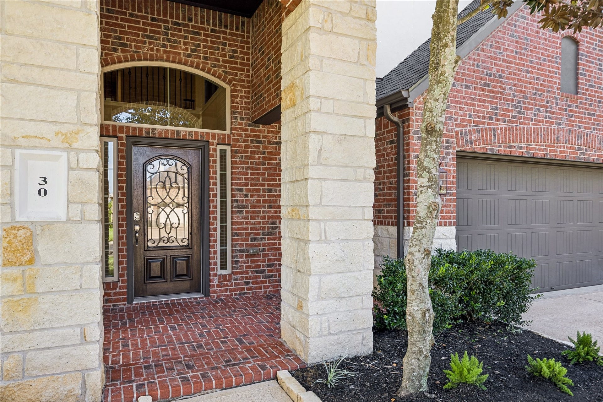 30 Glade Park Drive, Missouri City, TX 77459 Welcome home! A charming covered entry framed by stone columns and classic brickwork offers a warm welcome, while the beautiful front door with decorative ironwork and glass adds a touch of elegance before you even step inside.