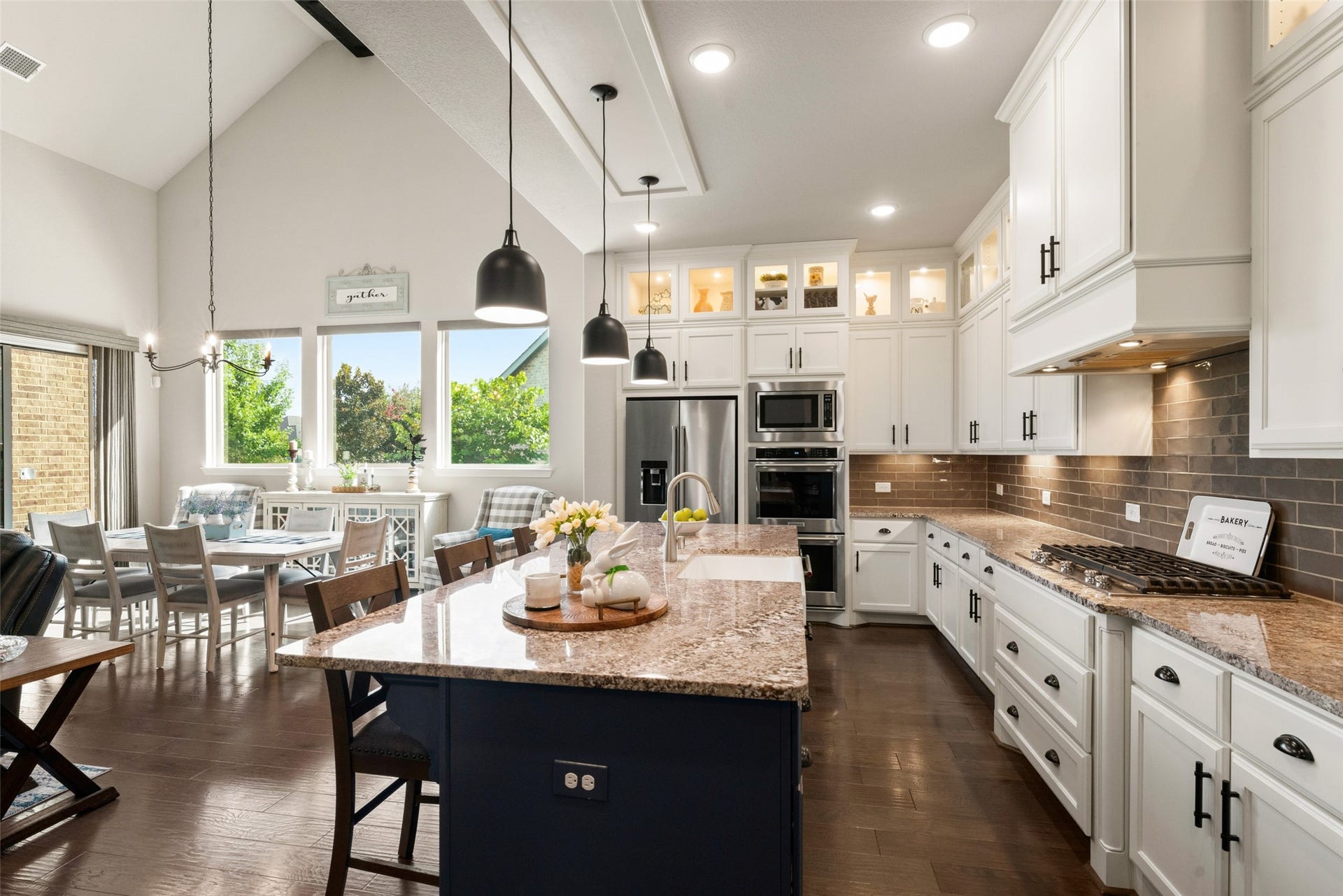23926 Arcola Glen Lane, Katy, TX 77493 Stunning kitchen featuring a dark blue dining island accented by silver pulls, contrasting crisp white wall cabinetry, with black pulls, and stylish black pendant lighting.