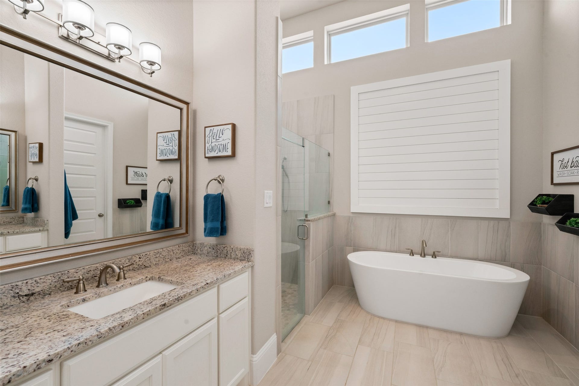 23926 Arcola Glen Lane, Katy, TX 77493 The primary bathroom features an upscale ambiance with an elegant tile-surround, free-standing soaking tub positioned beneath a large shuttered window, complemented by a spacious glass-enclosed walk-in shower.