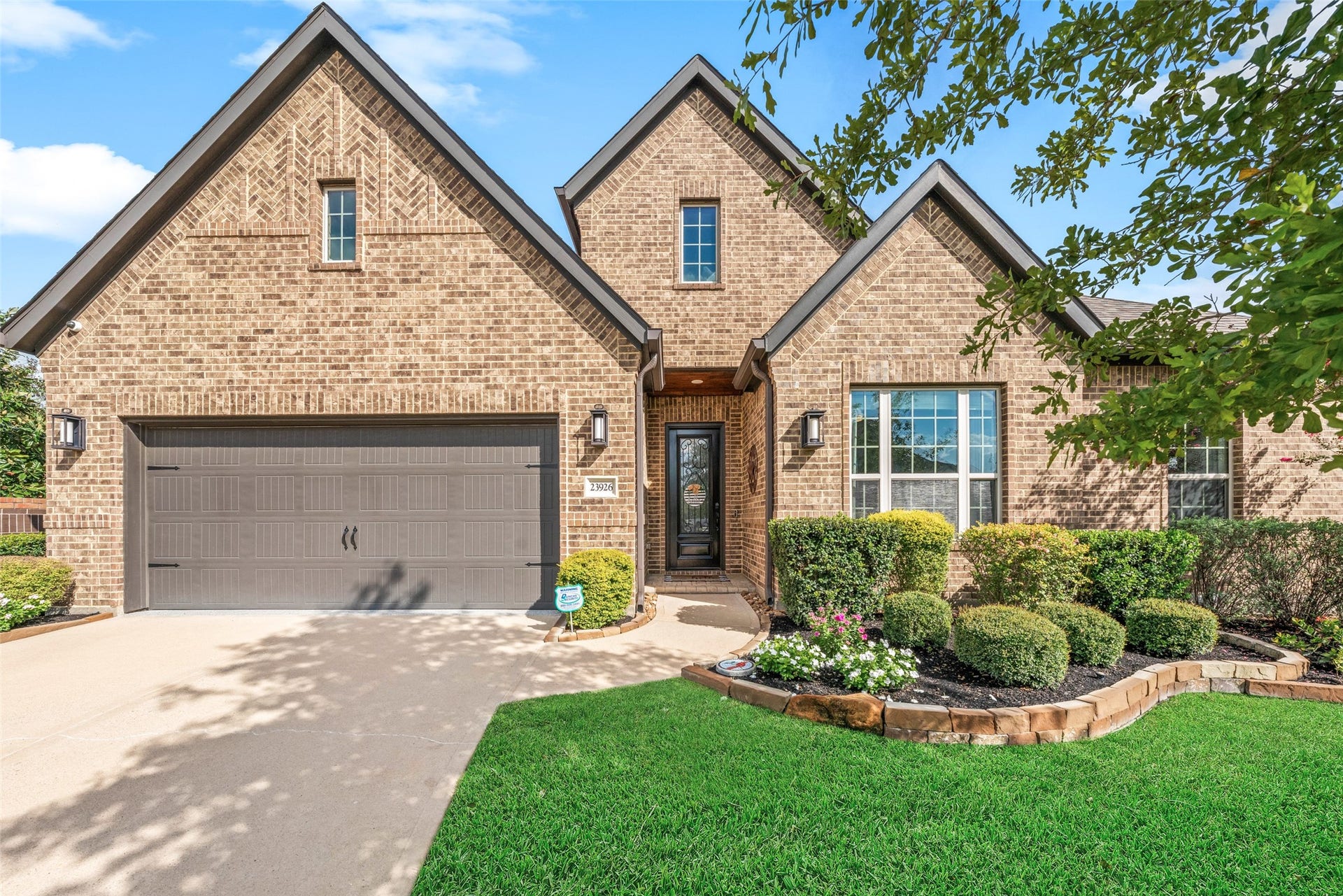 23926 Arcola Glen Lane, Katy, TX 77493 Stunning curb appeal featuring a light-toned brick exterior complemented by beautifully landscaped, rock-lined garden beds that add texture, color, and a warm, welcoming atmosphere.