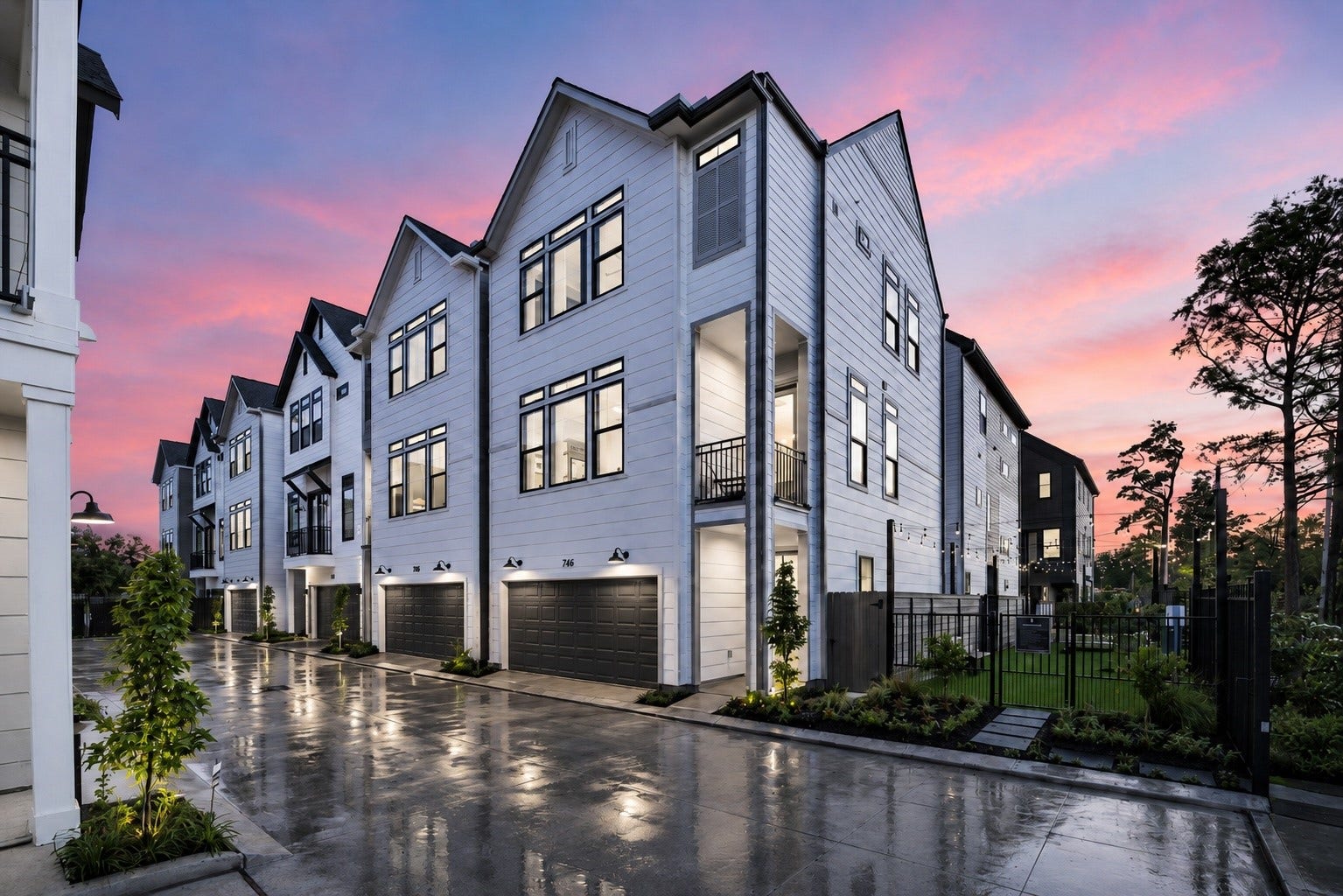 Modern townhomes with sleek white exteriors line a clean, well-lit street, set against a stunning sunset sky.