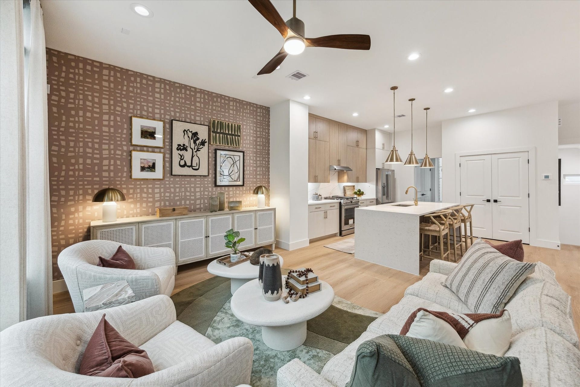 Experience modern elegance in this open-concept living space, featuring a stylish kitchen with an island, sleek cabinetry, and pendant lighting. The cozy sitting area is enhanced by a chic accent wall and contemporary decor, creating a perfect blend of comfort and sophistication.