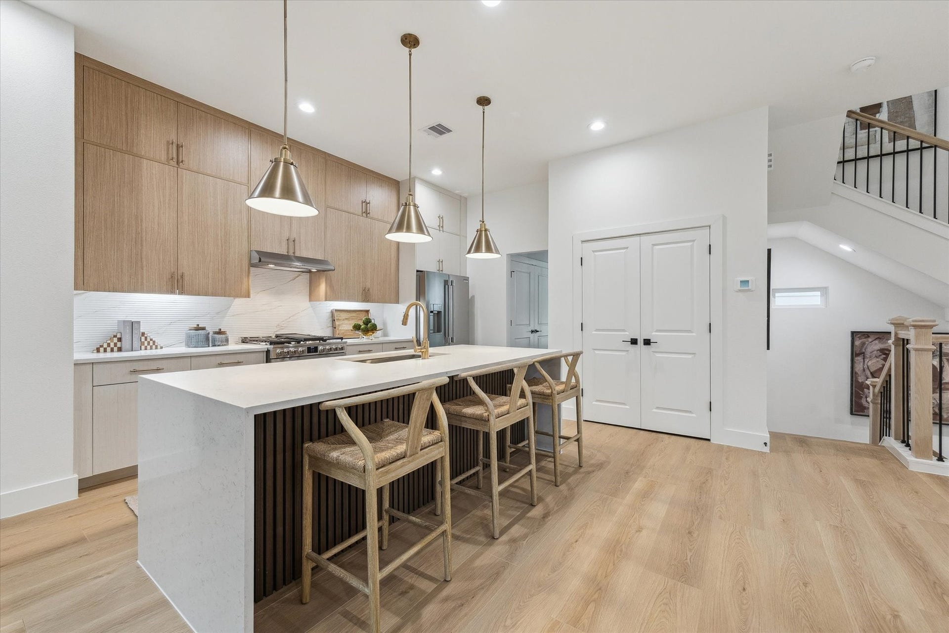 Sleek modern kitchen with a spacious island, pendant lighting, and stylish wood cabinetry, complemented by stainless steel appliances and warm wood flooring.