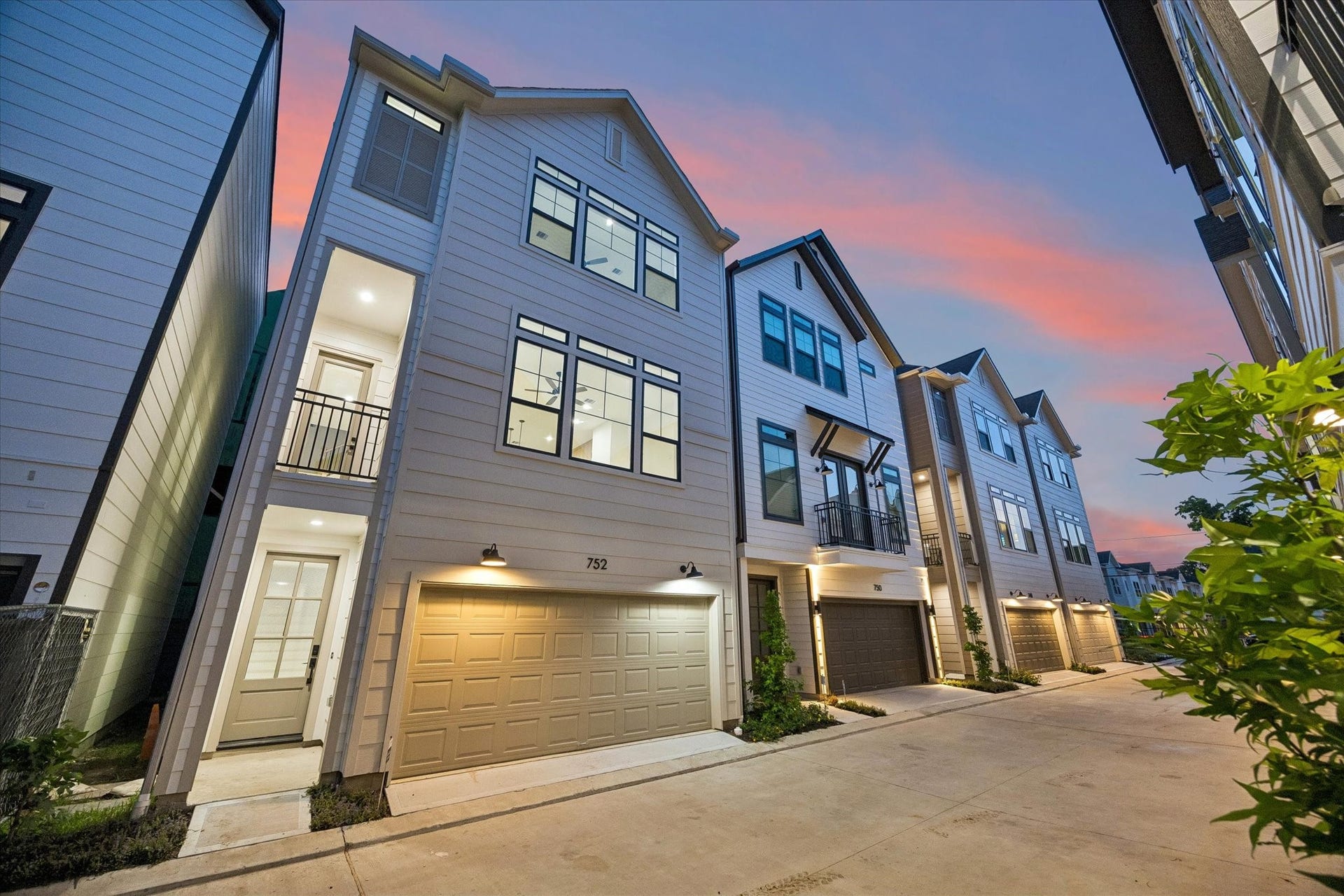 Modern three-story townhomes with spacious garages and large windows, set against a picturesque sunset sky.