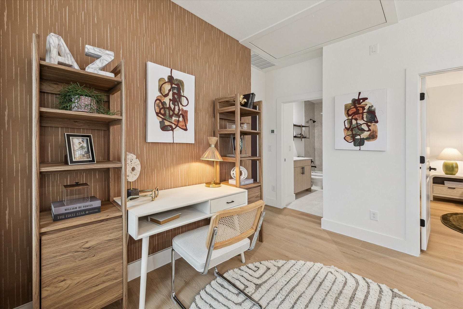 Charming home office with stylish wood shelving, a contemporary desk, and chic artwork. The space is bright and inviting, leading to adjacent rooms for seamless functionality.