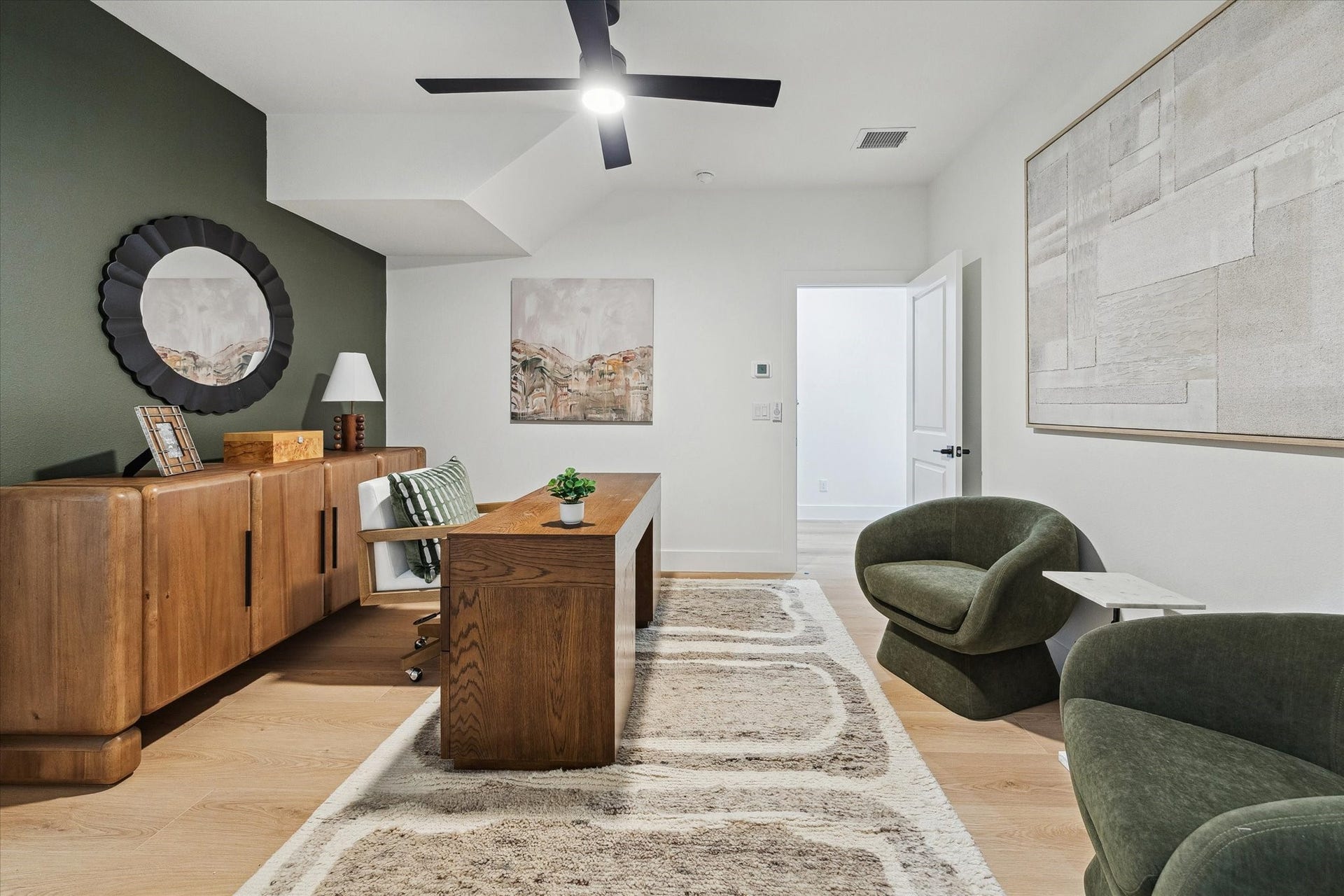 Elegant home office with a modern wooden desk, plush seating, and stylish decor, complemented by a sleek ceiling fan and natural light.