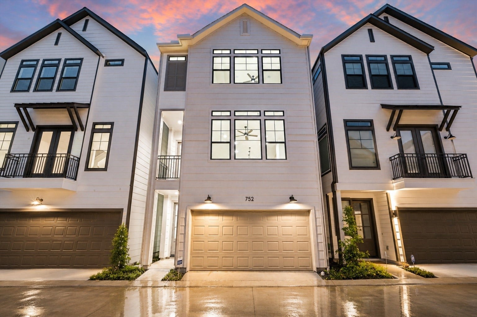 Modern three-story townhouse with elegant black trim, spacious windows, and a two-car garage, set against a vibrant sunset sky.