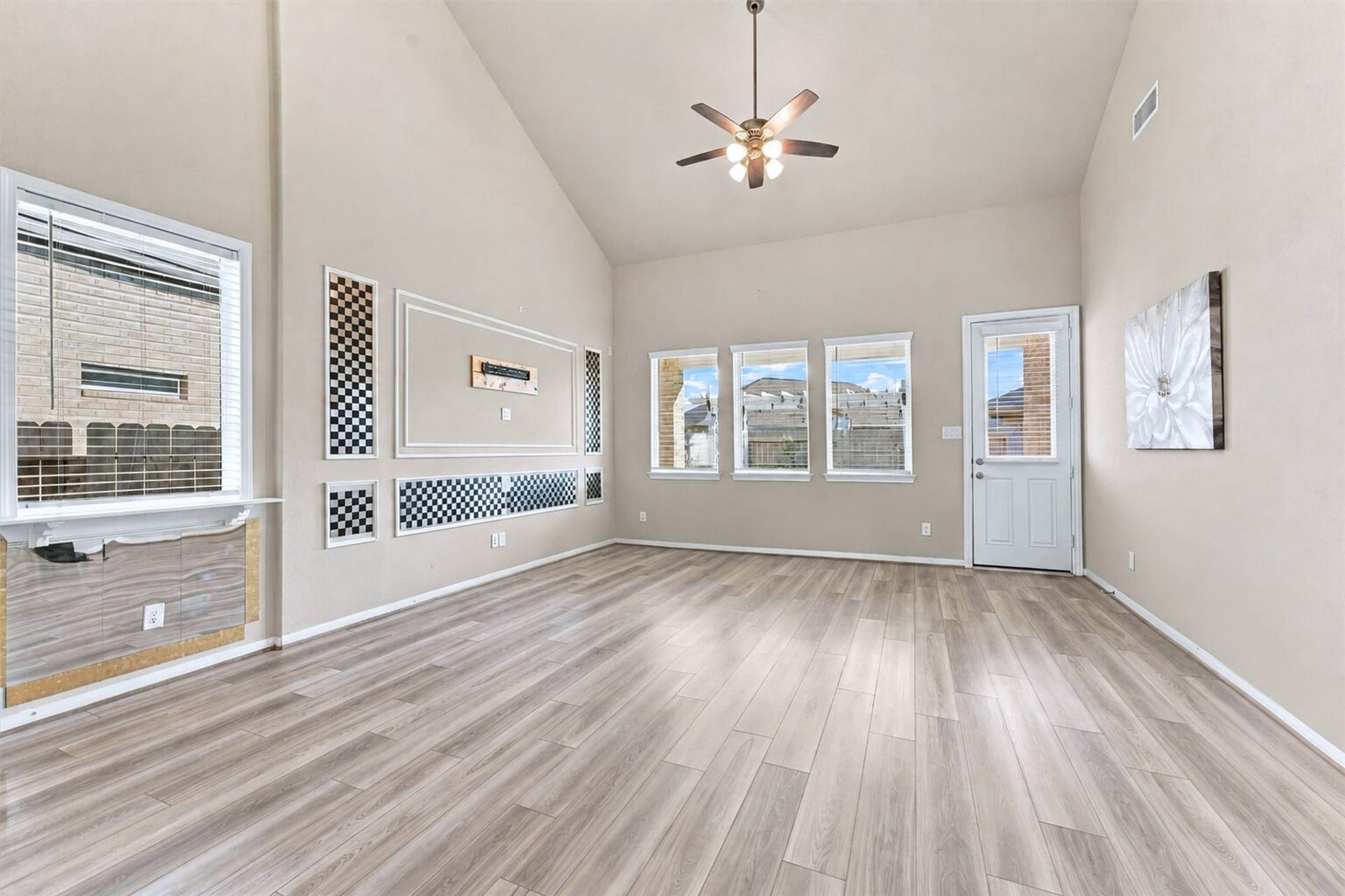 Spacious living room featuring soaring vaulted ceilings, abundant natural light, decorative wall accents, and wood-look flooring.