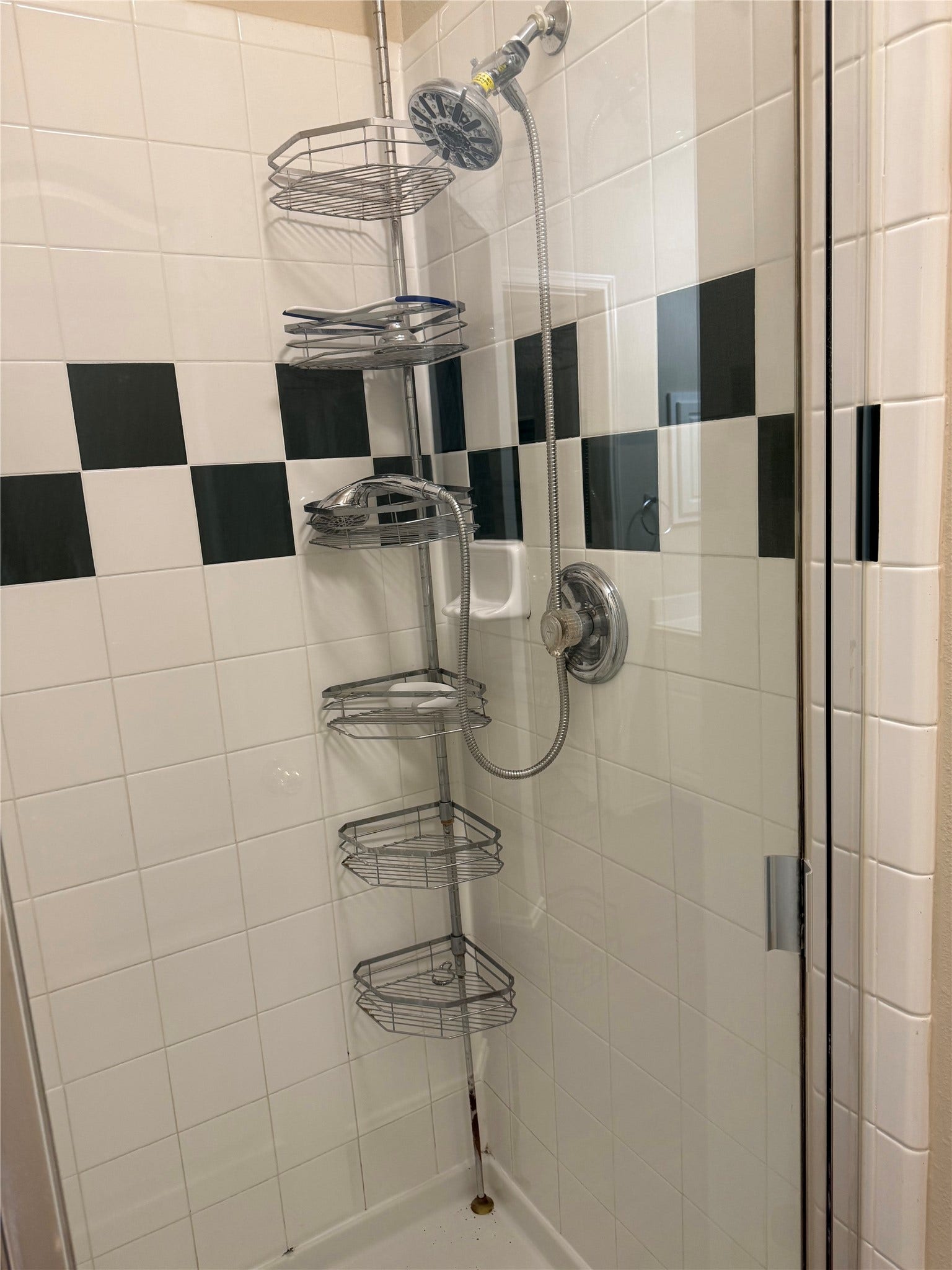 2104 Goldfinch Lane, League City, TX 77573 Modern shower with sleek chrome fixtures, glass door, and convenient storage shelves, set against a classic black and white tiled backdrop.