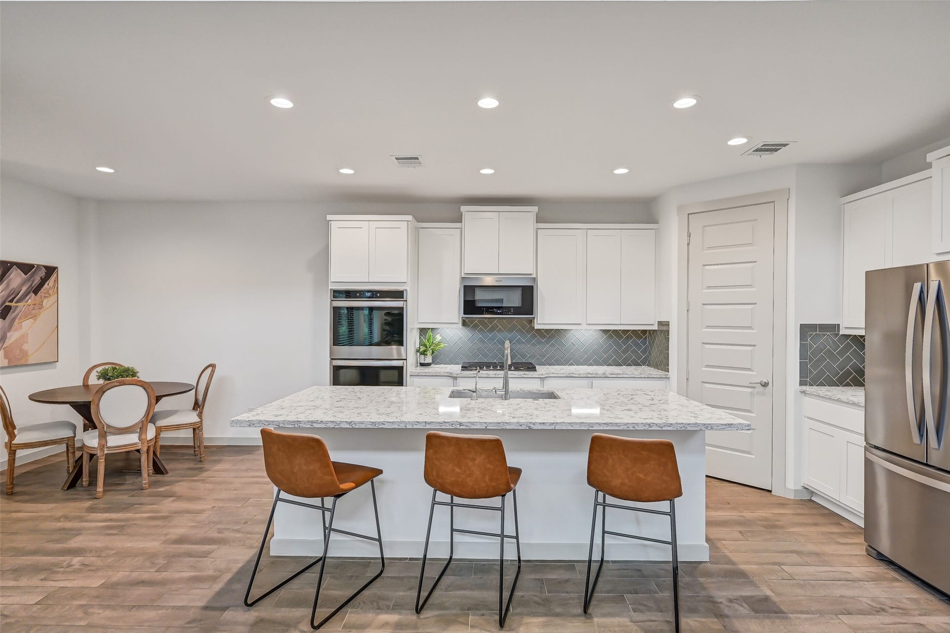 1570 Mustang Trail, Friendswood, TX 77546 The showpiece kitchen centers around an oversized quartz island with generous seating and prep space, complemented by crisp white shaker cabinetry, stainless appliances, recessed lighting, and a stylish herringbone tile backsplash.