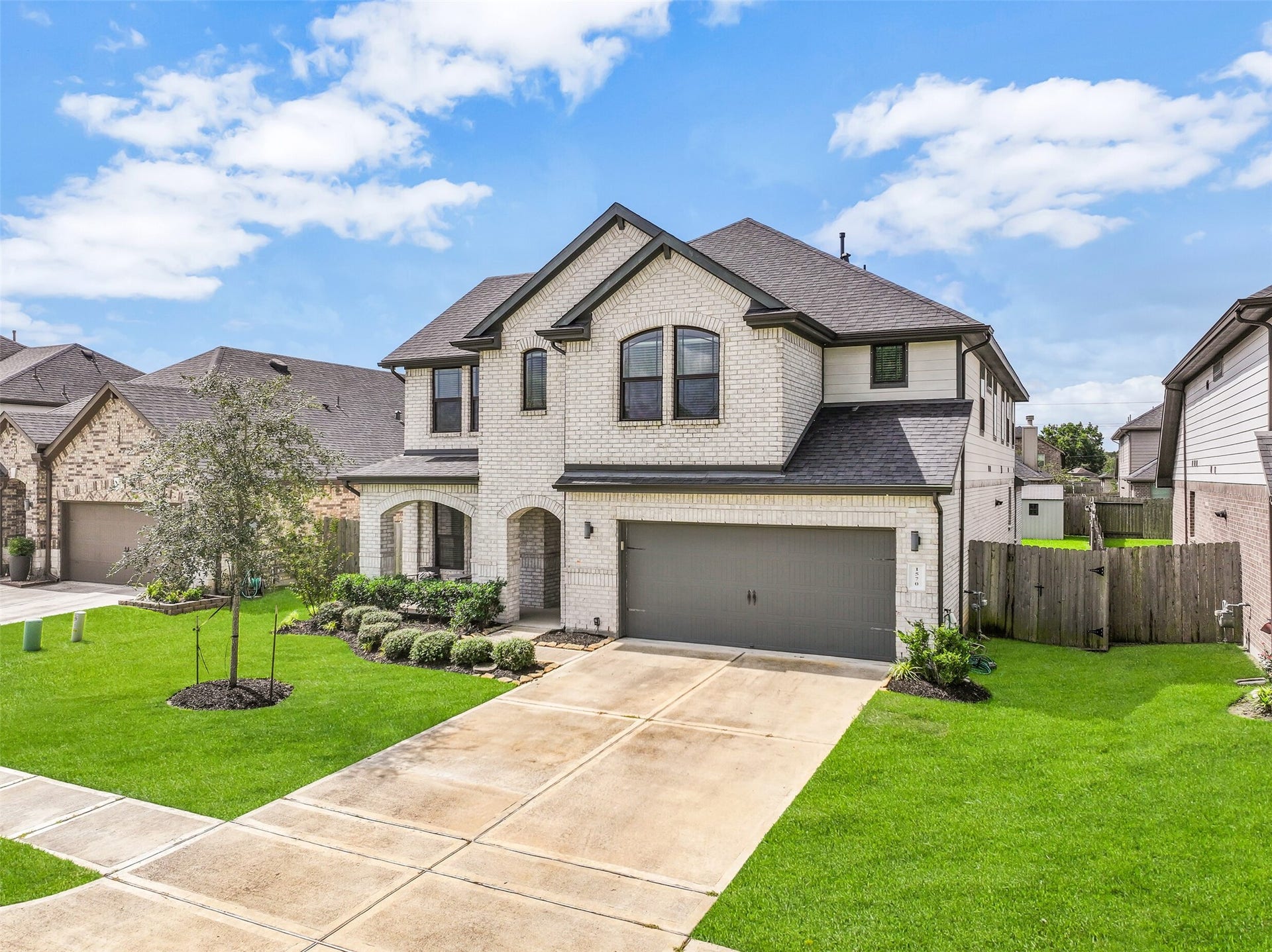 1570 Mustang Trail, Friendswood, TX 77546 Another look at this impressive two-story home highlights its striking brick elevation, neatly landscaped front yard, double-wide driveway, and attached garage with a rare tandem third bay providing additional parking or storage space.