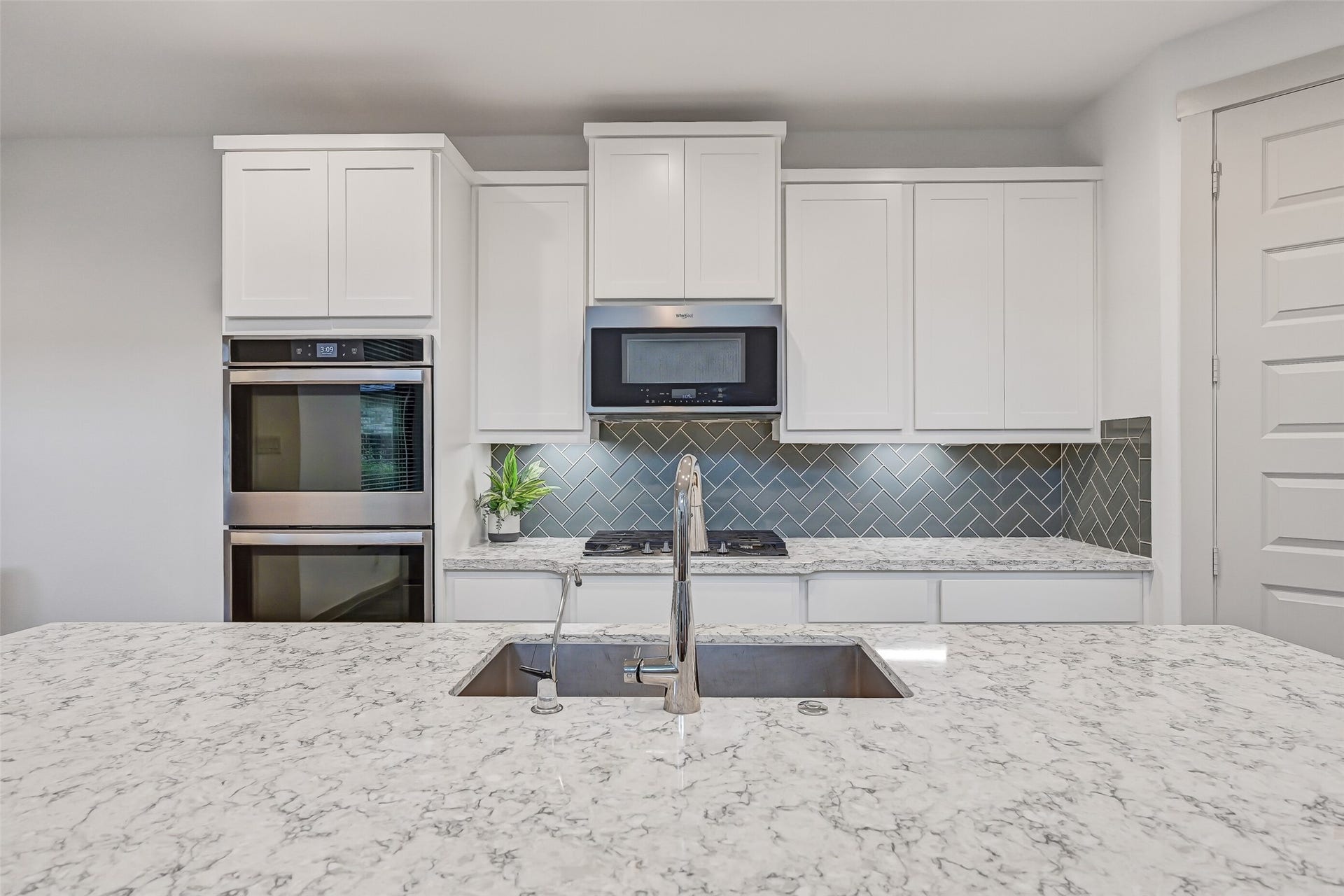 1570 Mustang Trail, Friendswood, TX 77546 This angle highlights the impressive size of the quartz-topped island, offering plenty of room for meal prep, serving, and casual seating. White shaker cabinetry, stainless appliances, and a sleek tile backsplash complete the bright, contemporary design.