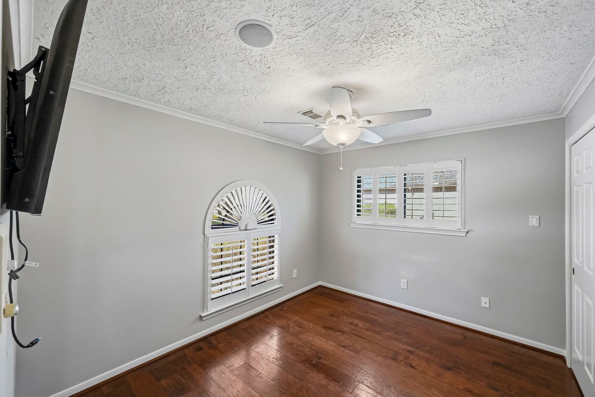 9354 Escondido Drive, Willis, TX 77318 Bedroom #3 features wood-look tile flooring, crown molding, a ceiling fan and a charming arched window with plantation shutters.