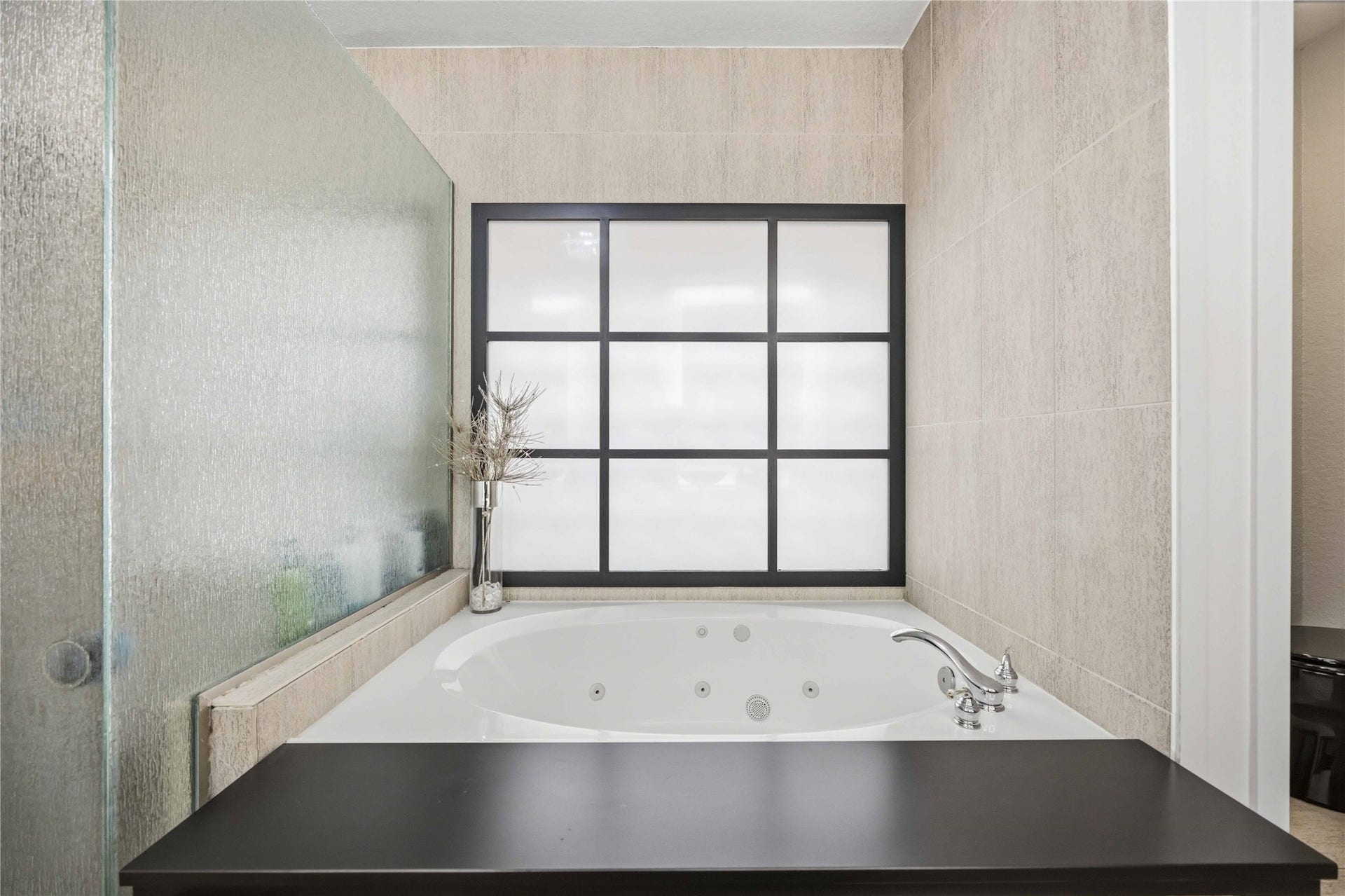 7610 Guinevere Drive, Sugar Land, TX 77479 A close-up of the bathing alcove emphasizes the jetted tub's custom dark ledge wrapper and the stone-textured wall tiling.