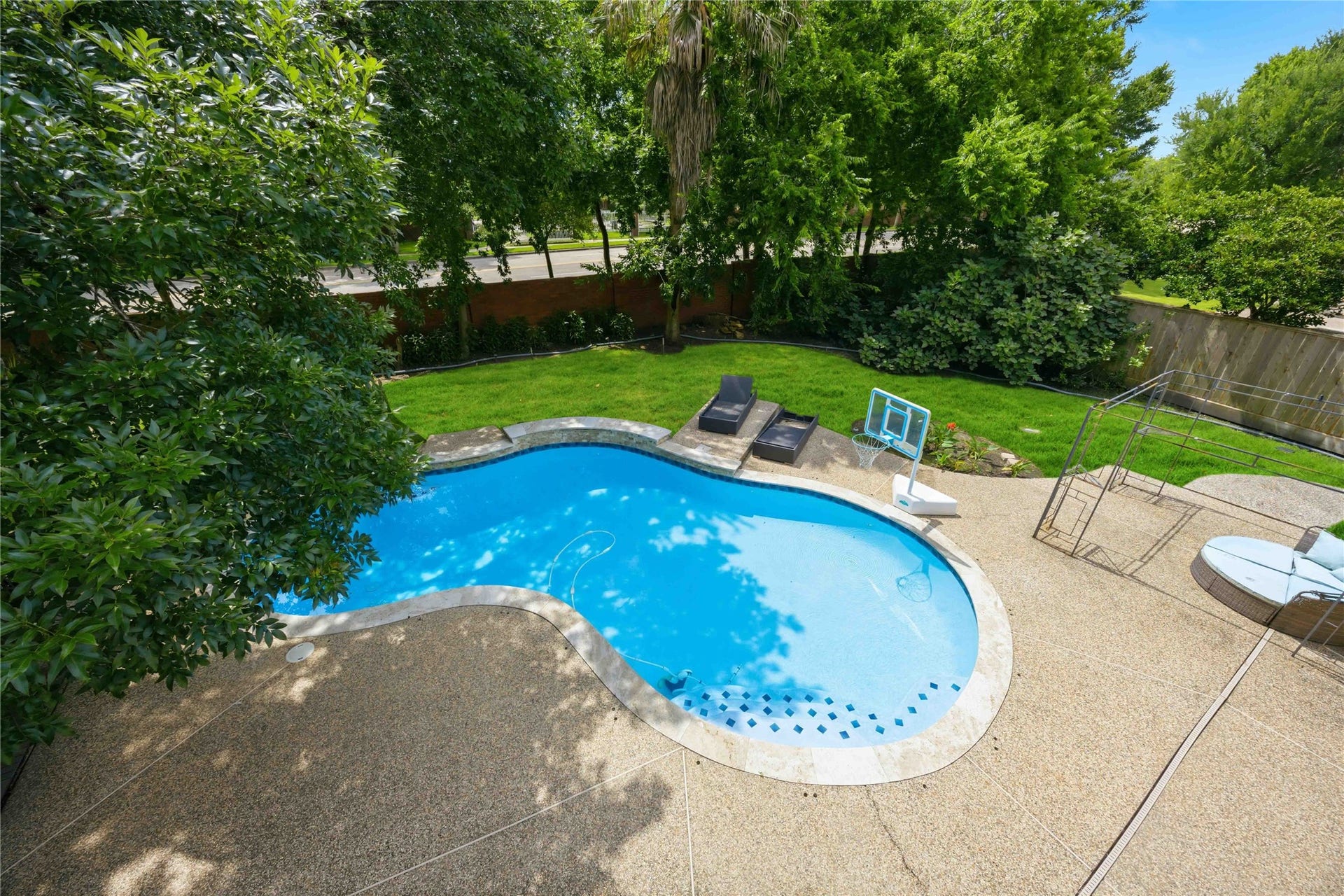 7610 Guinevere Drive, Sugar Land, TX 77479 An elevated bird's-eye view reveals a custom curved in-ground swimming pool framed by an expansive concrete aggregate patio surround.