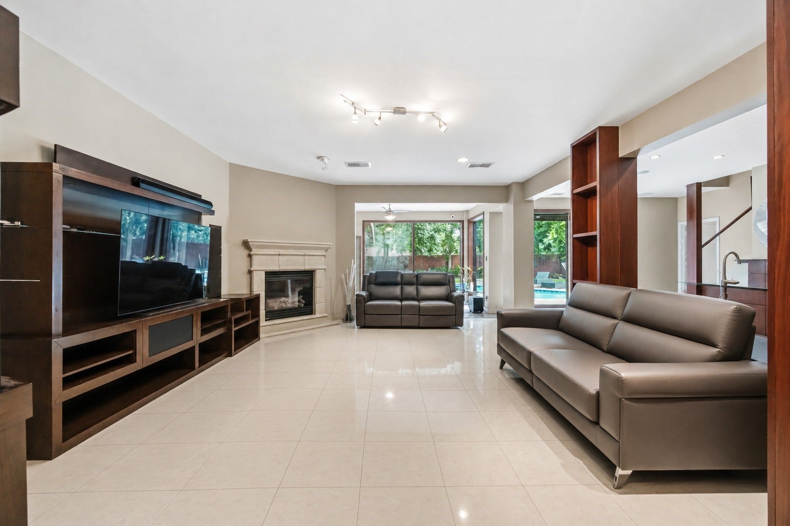 7610 Guinevere Drive, Sugar Land, TX 77479 This expansive living room features a corner gas fireplace with a stone-style mantle, polished tile flooring, and integrated dark wood shelving.
