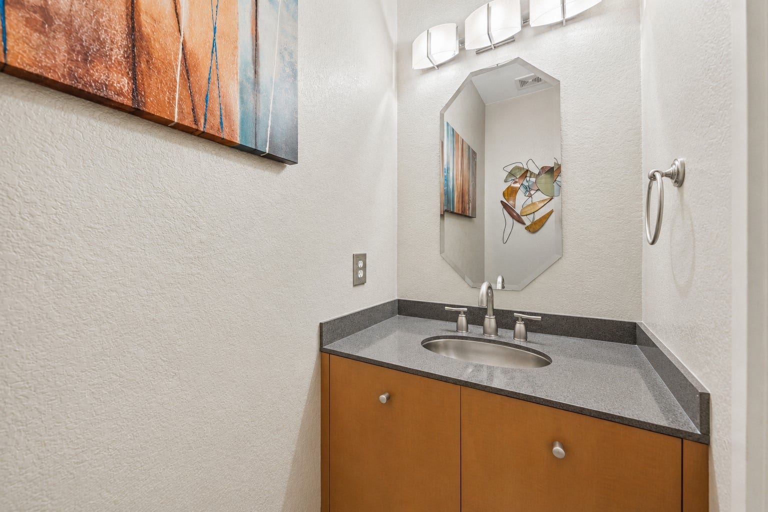 7610 Guinevere Drive, Sugar Land, TX 77479 The powder room features a warm wood vanity cabinet topped with a gray stone counter, an under-mount sink, and a modern three-light wall fixture.