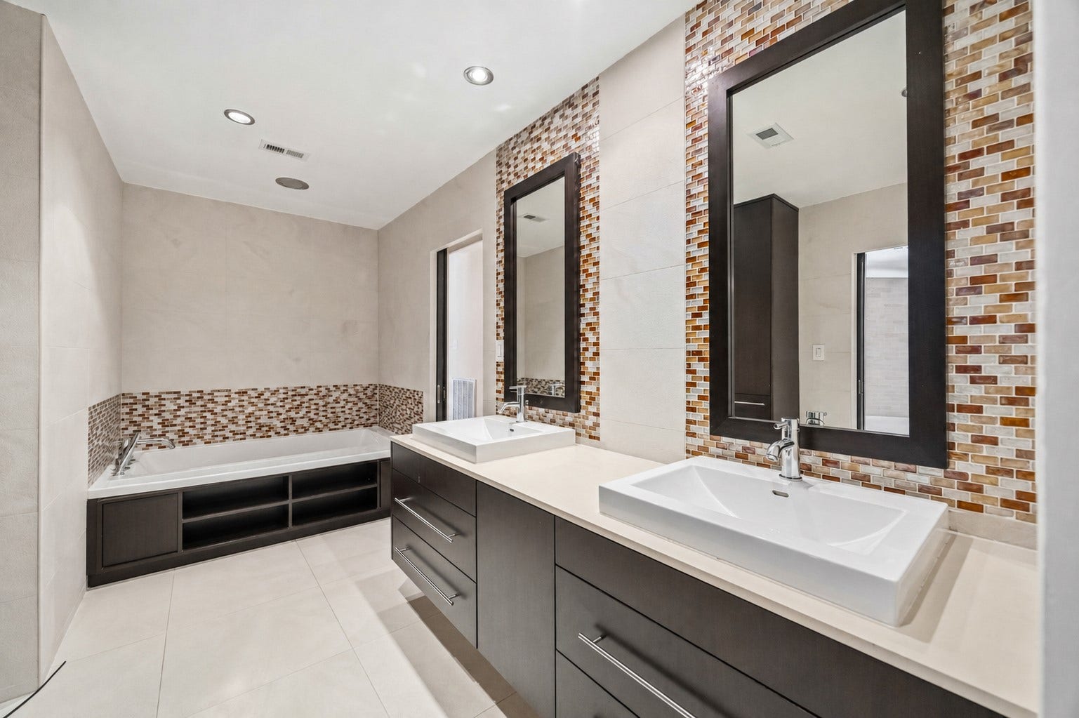 7610 Guinevere Drive, Sugar Land, TX 77479 Modern full bath with a deep soaking tub, built-in shelving, dual vessel-sink vanities, and colorful mosaic tile accents.