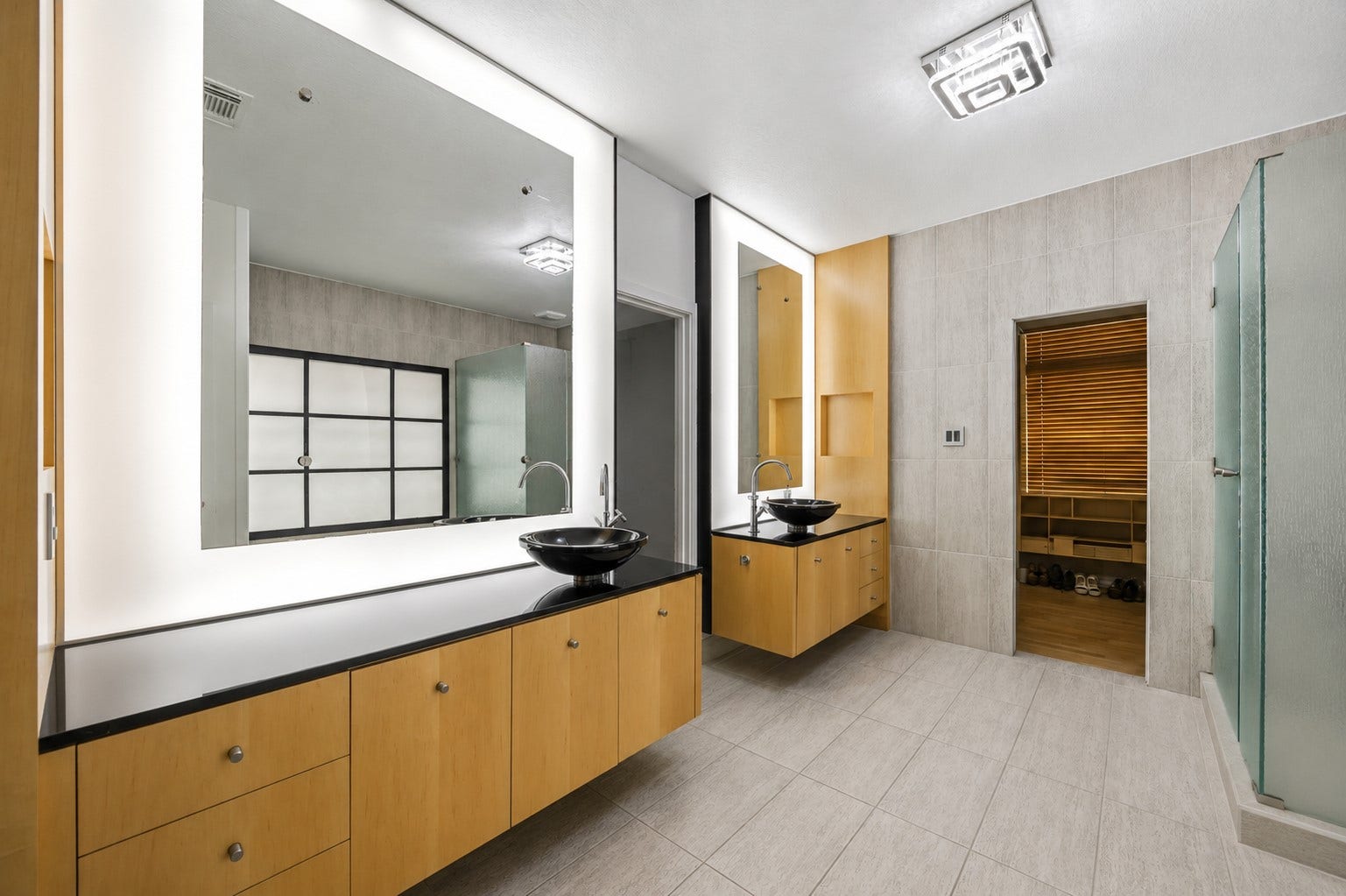 7610 Guinevere Drive, Sugar Land, TX 77479 This modern bathroom showcases dual floating vanities with light wood cabinetry, sleek black countertops with vessel sinks, and integrated back-lit mirrors.