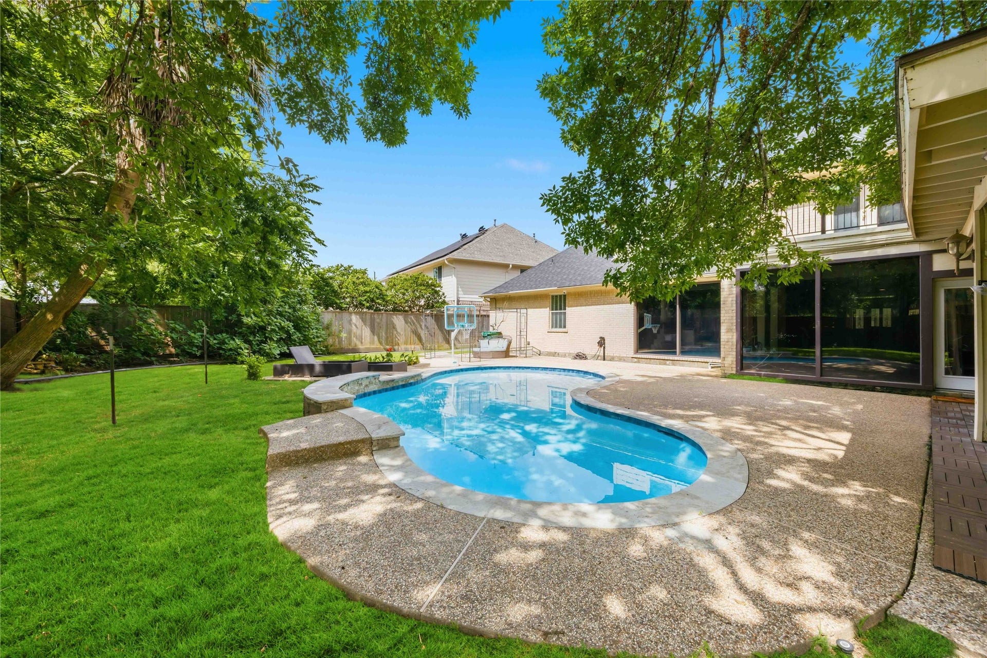 7610 Guinevere Drive, Sugar Land, TX 77479 A wide lush lawn borders the custom swimming pool, bordered by mature trees and privacy wood fencing.