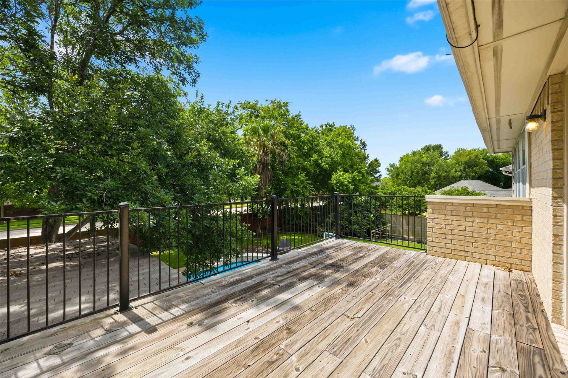 7610 Guinevere Drive, Sugar Land, TX 77479 An upper-level wooden sun deck features a black metal safety railing and views overlooking the backyard greenery.