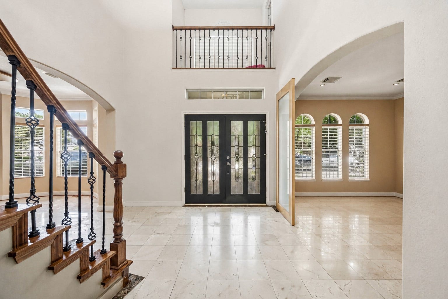 7610 Guinevere Drive, Sugar Land, TX 77479 A soaring two-story foyer highlights a dramatic black double-door entry with decorative glass panels, an overhead balcony railing, and large multi-paned windows that fill the space with light.