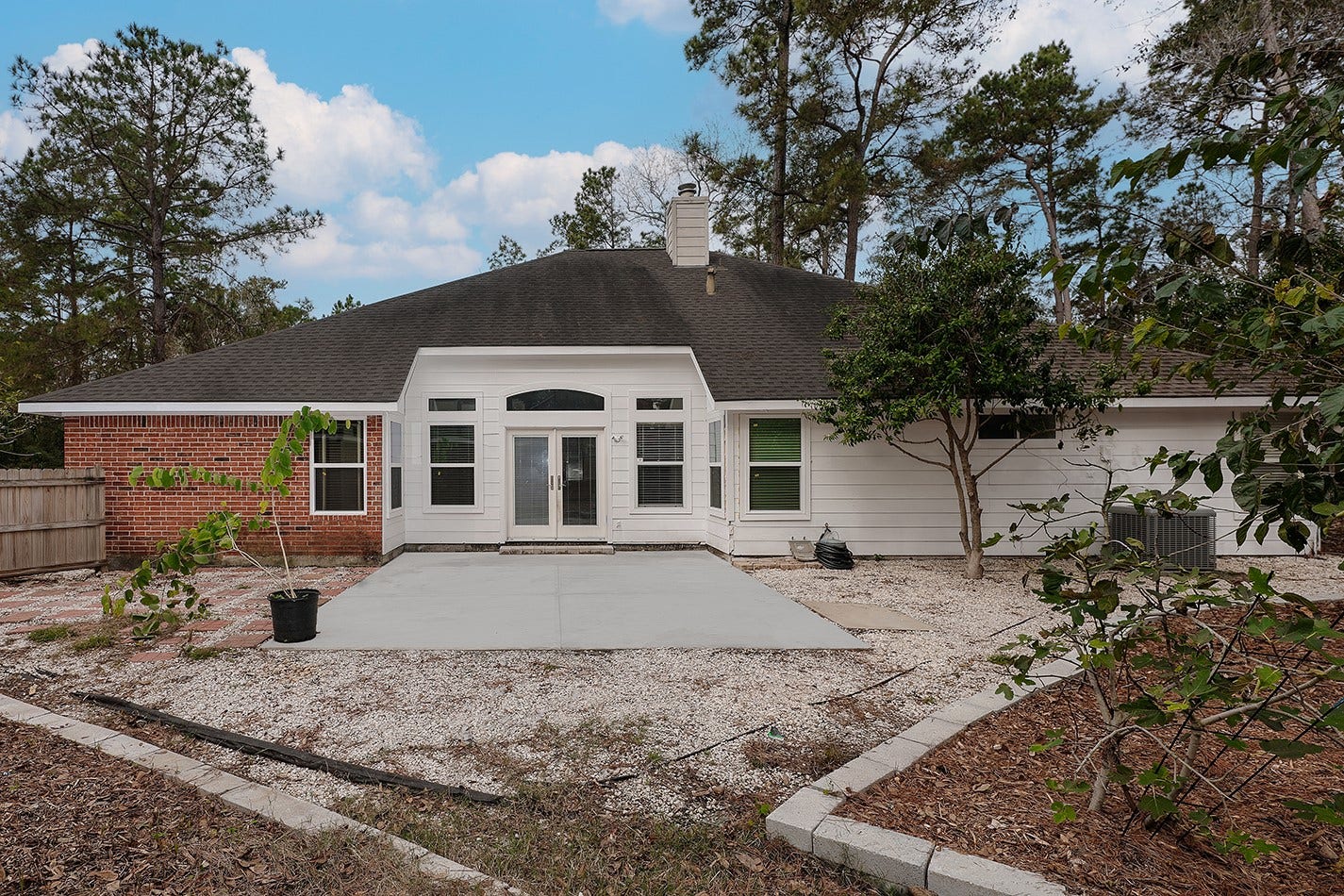 34 Cypress Bayou Court, The Woodlands, TX 77382 The back yard features a spacious concrete patio, surrounded by a low-maintenance landscape with trees and a wooden fence, providing a private and serene outdoor space.