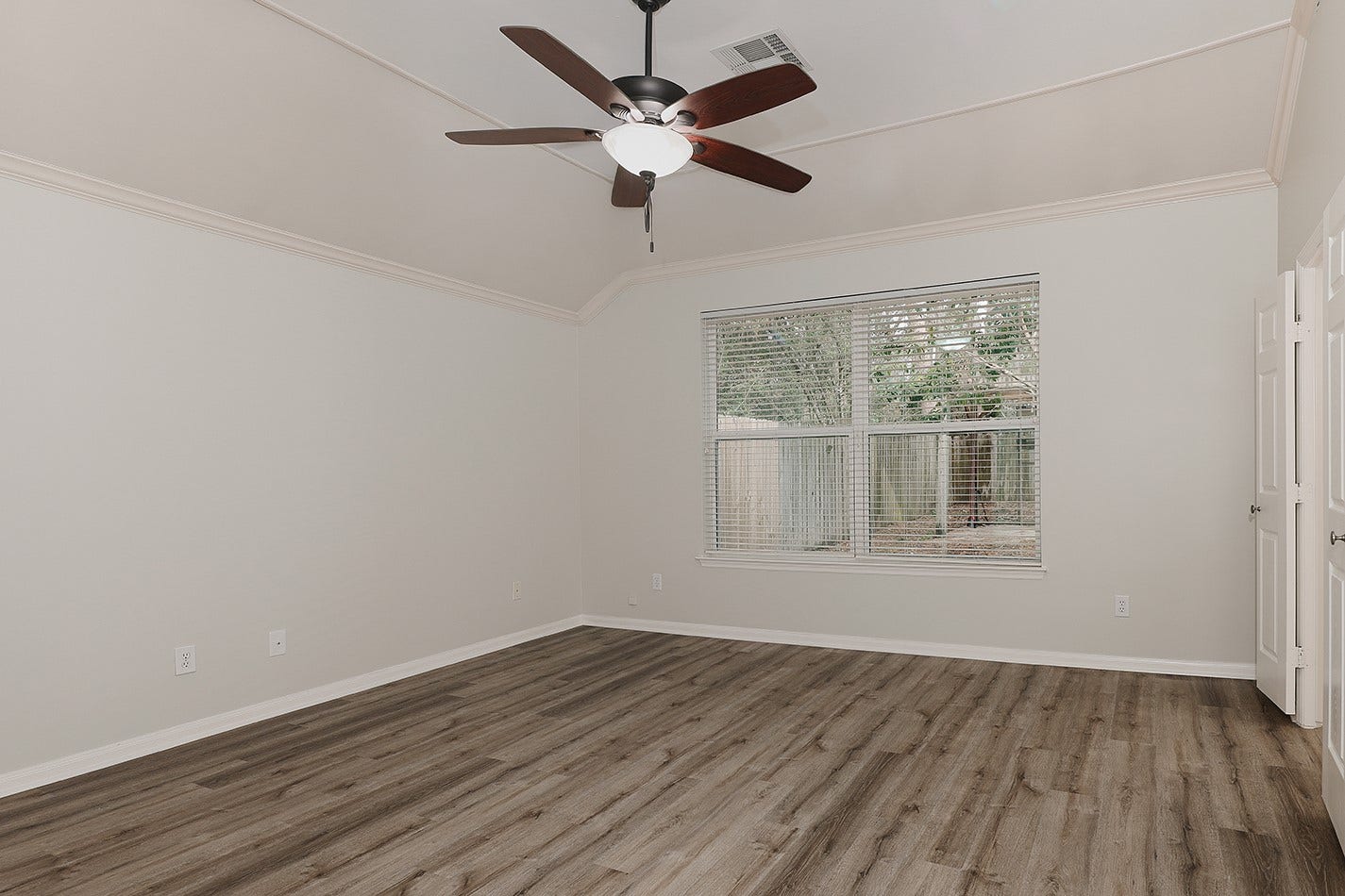 34 Cypress Bayou Court, The Woodlands, TX 77382 This spacious room features light-colored walls, wood-style flooring, a ceiling fan, and a large window offering natural light and garden views.