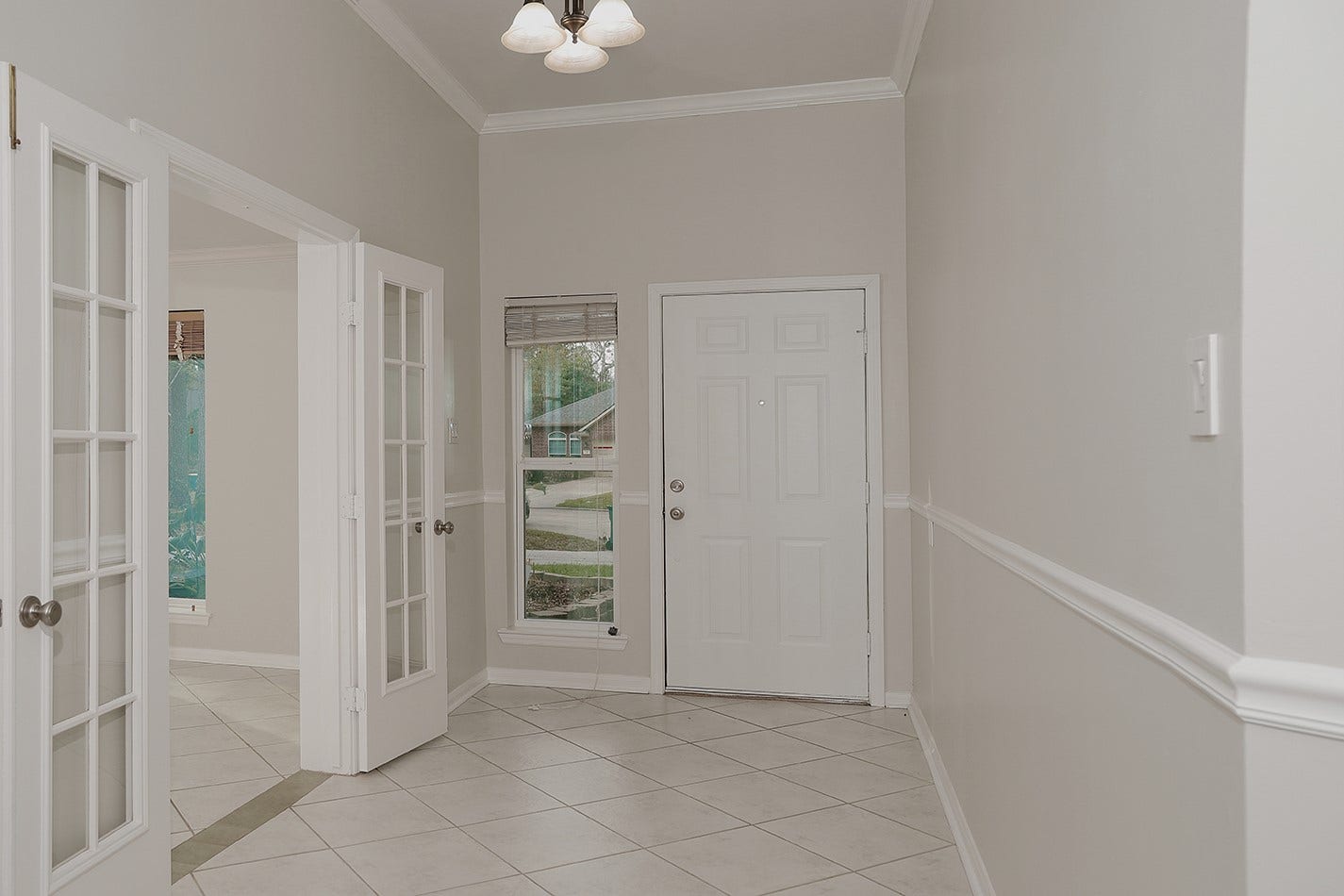 34 Cypress Bayou Court, The Woodlands, TX 77382 A welcoming entryway with neutral tones, featuring a tiled floor, crown molding, and French doors leading to the study.