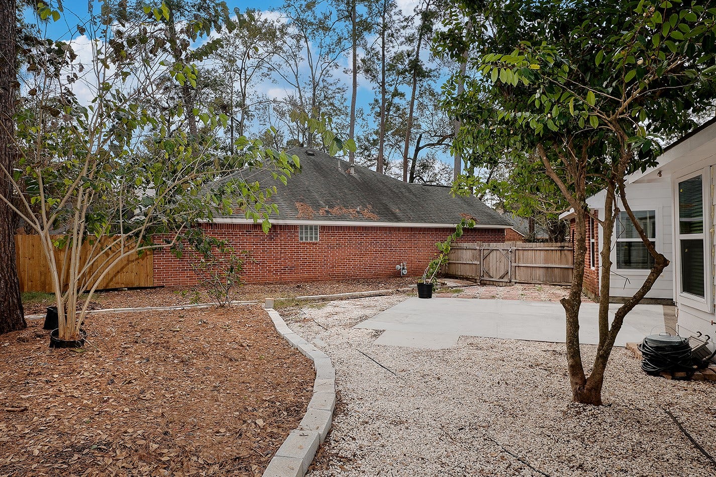 34 Cypress Bayou Court, The Woodlands, TX 77382 The spacious backyard has a mix of gravel and mulch landscaping, featuring mature trees and a patio area.