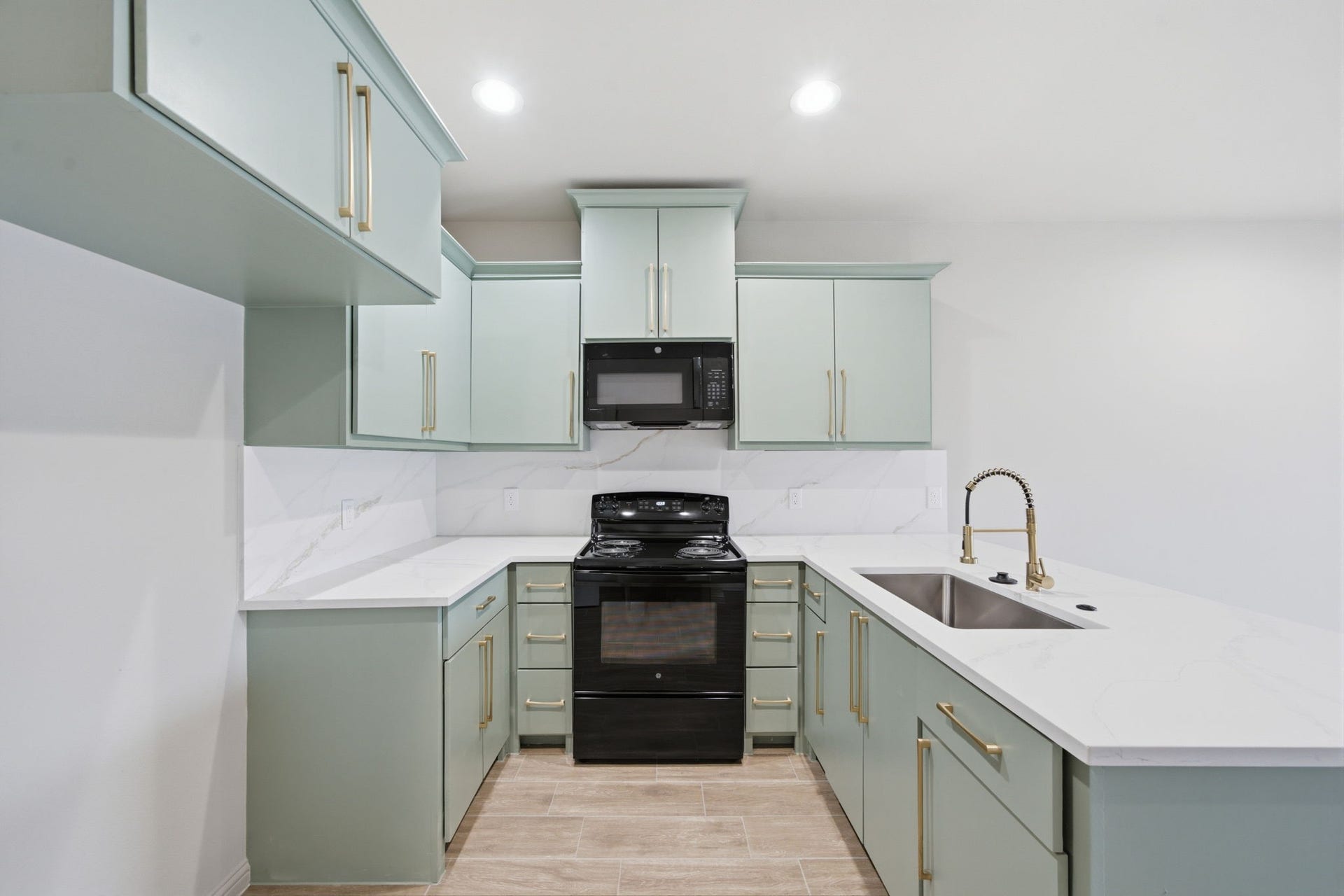 Modern kitchen features soft sage cabinetry, quartz countertops, warm brass hardware and a generous peninsula with seating potential.