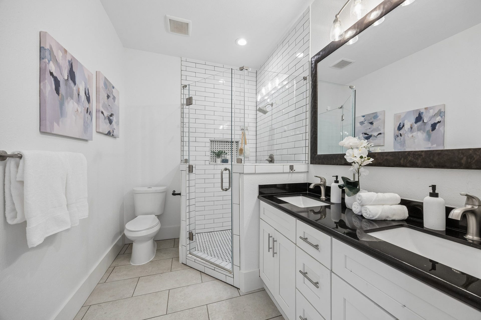 711 4th Street, Sealy, TX 77474 Sleek and modern bathroom featuring a glass-enclosed shower with subway tile, dual-sink vanity with black countertops and elegant fixtures.