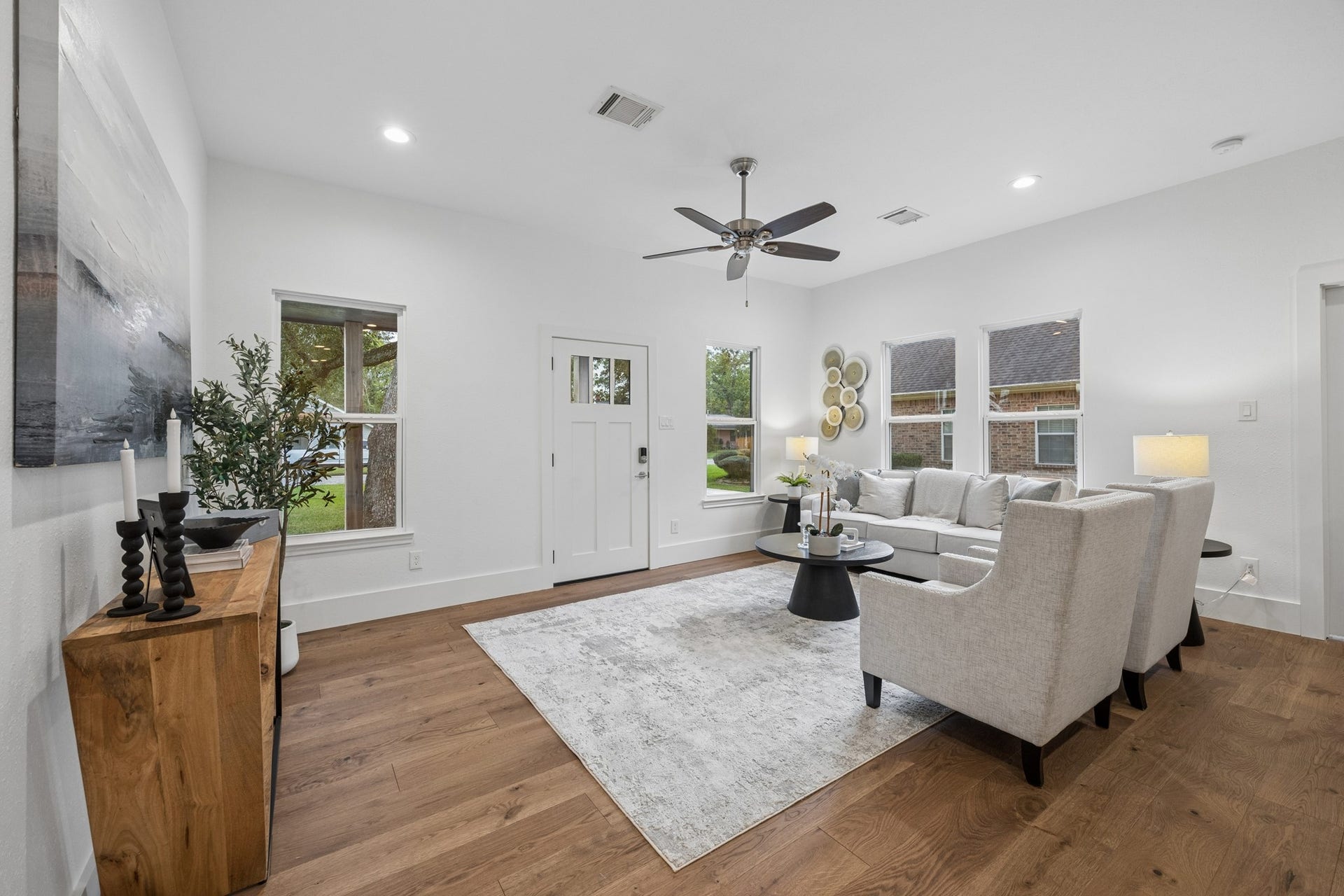711 4th Street, Sealy, TX 77474 Bright and inviting living room featuring a stylish ceiling fan, elegant wood flooring, and ample natural light from multiple windows.