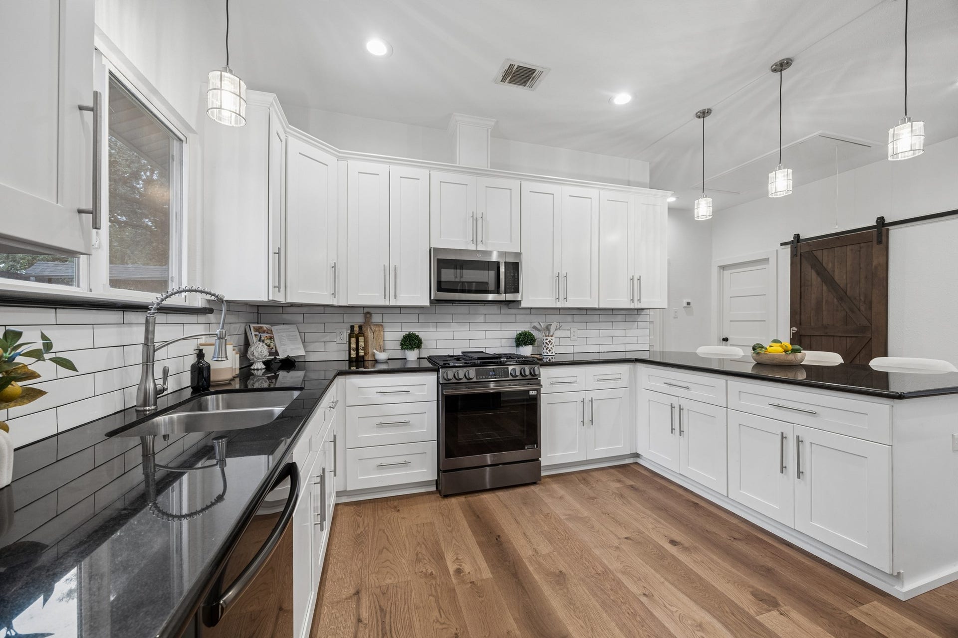 711 4th Street, Sealy, TX 77474 Spacious kitchen with sleek white cabinetry, new stainless steel appliances, and a spacious black countertop. The open layout features a barn door and pendant lighting, complemented by a bright, airy atmosphere and warm wood flooring.
