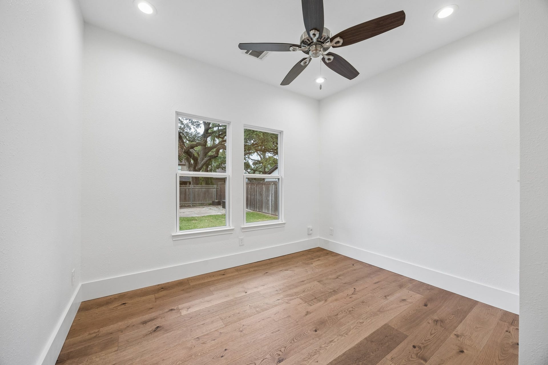 711 4th Street, Sealy, TX 77474 Bedroom featuring elegant hardwood floors, recessed lighting, and a ceiling fan, with large windows offering a view of the lush backyard.