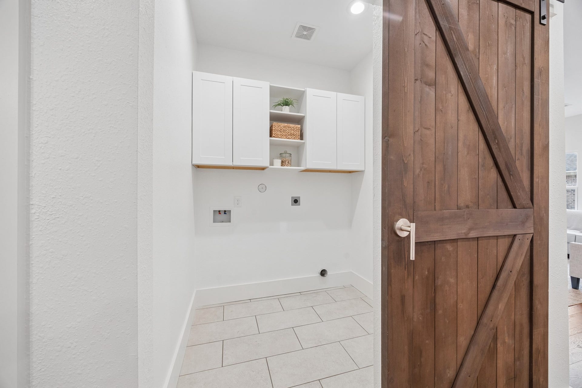 711 4th Street, Sealy, TX 77474 Convenient laundry room with sleek white cabinets and rustic wooden barn door, offering both style and functionality.