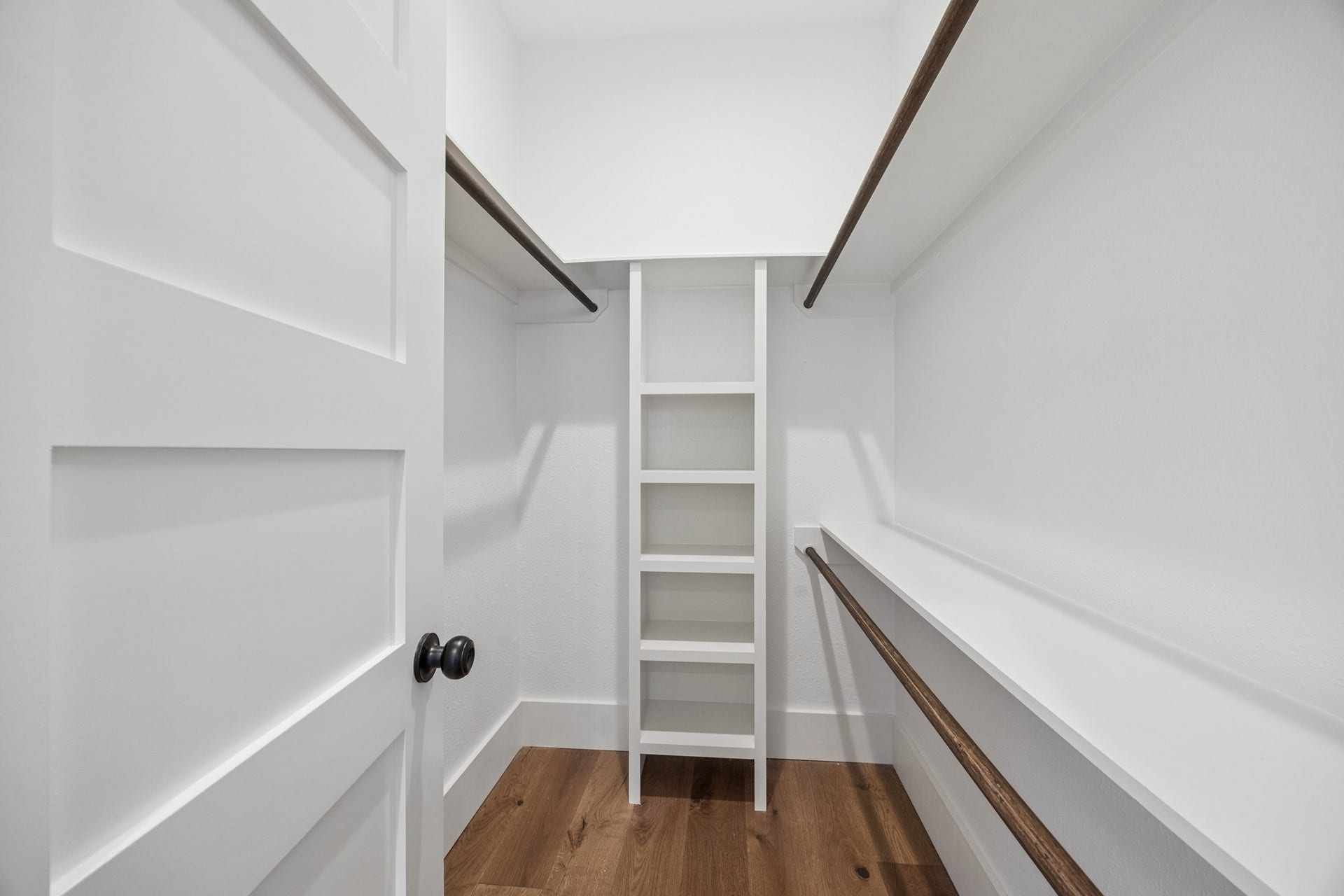 711 4th Street, Sealy, TX 77474 Spacious walk-in closet featuring elegant built-in shelving and rich wooden floors, offering ample storage space.