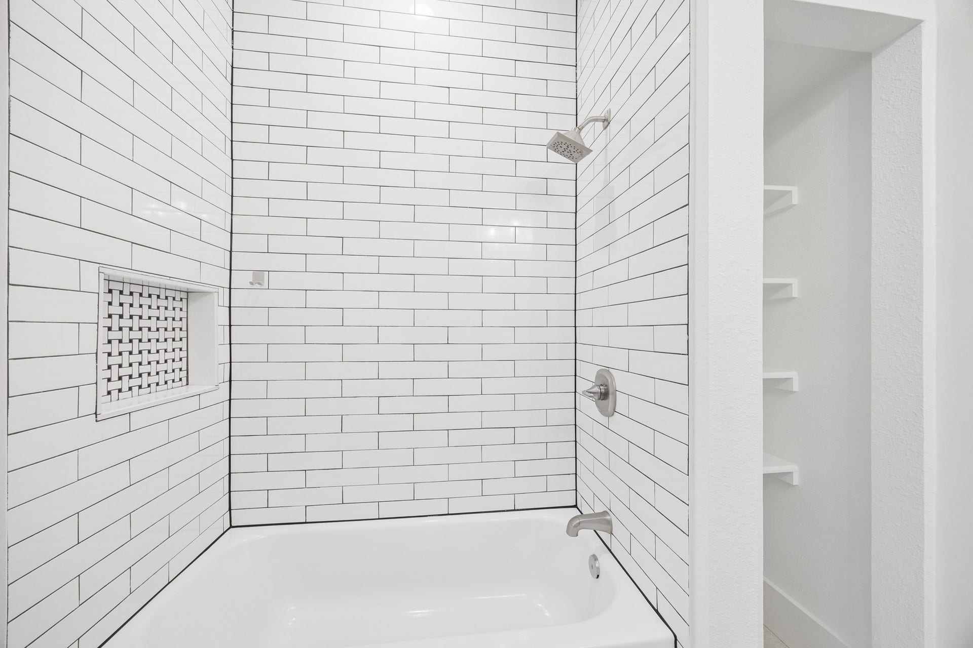 711 4th Street, Sealy, TX 77474 Sleek bathroom featuring a modern white subway tile design, spacious tub, and built-in shelving for convenient storage.