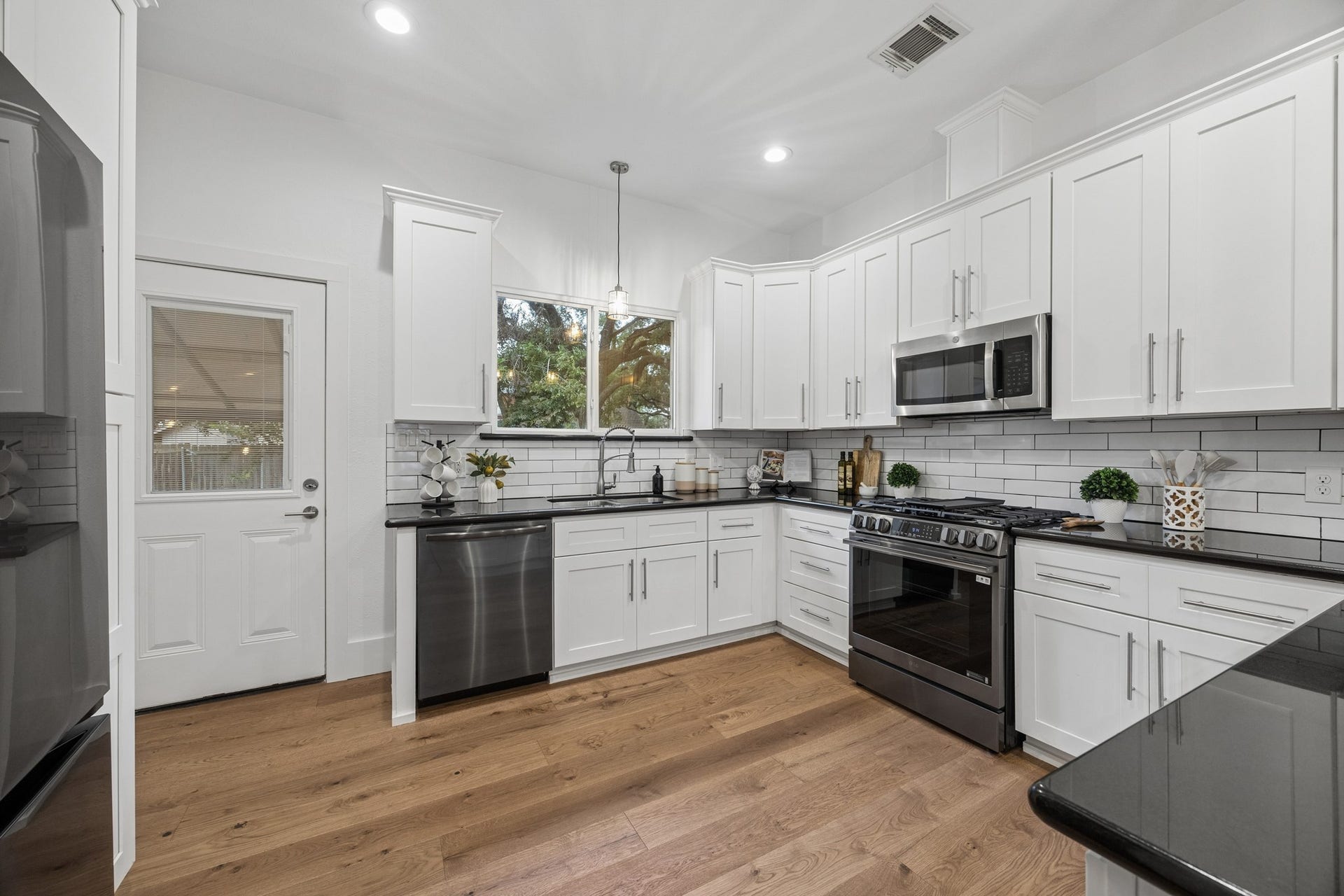 711 4th Street, Sealy, TX 77474 Bright and modern kitchen with sleek white cabinetry, stainless steel appliances, and elegant subway tile backsplash, complemented by warm hardwood floors.