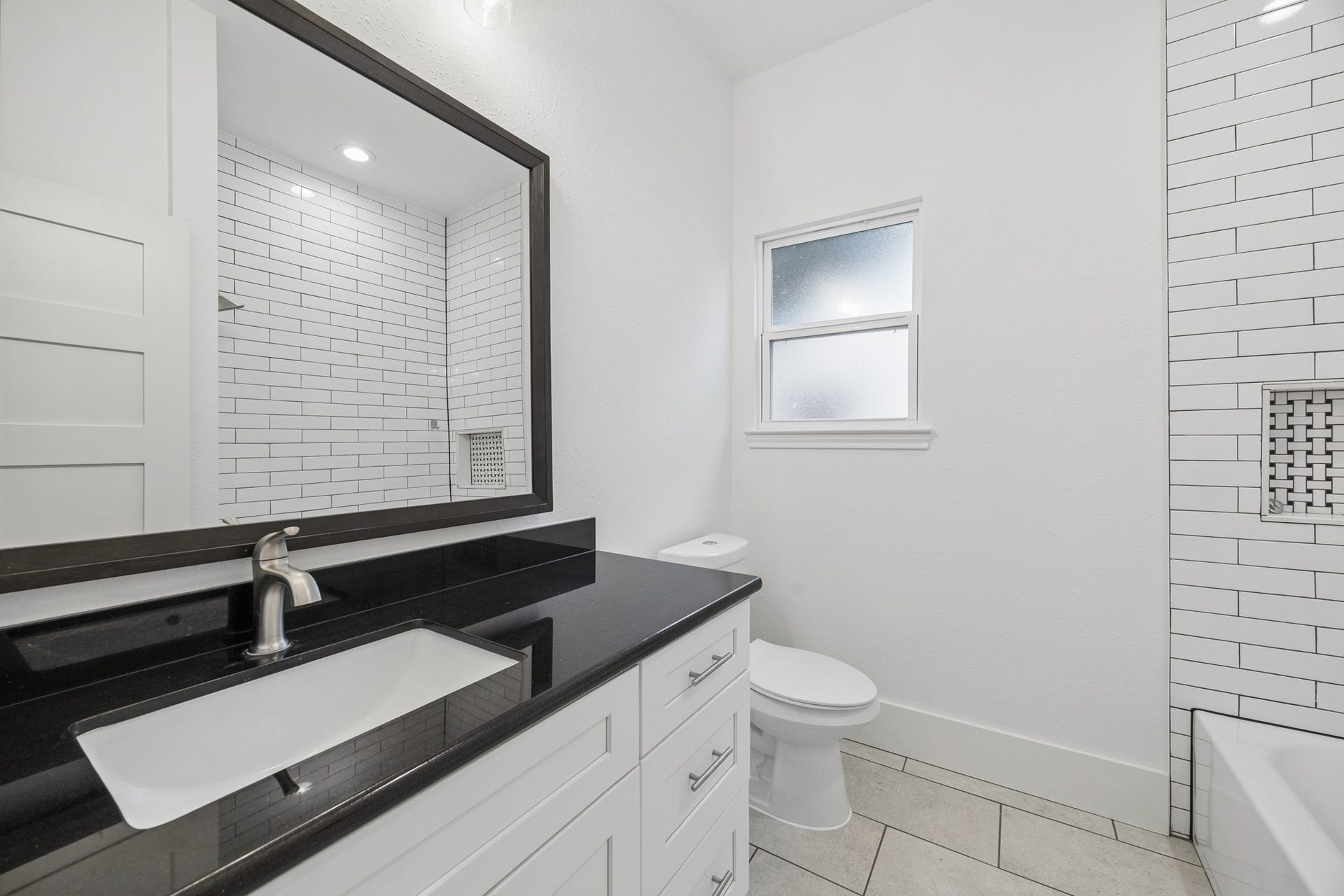 711 4th Street, Sealy, TX 77474 Sleek bathroom featuring a modern black countertop, stylish white cabinetry, and elegant subway tile accents.
