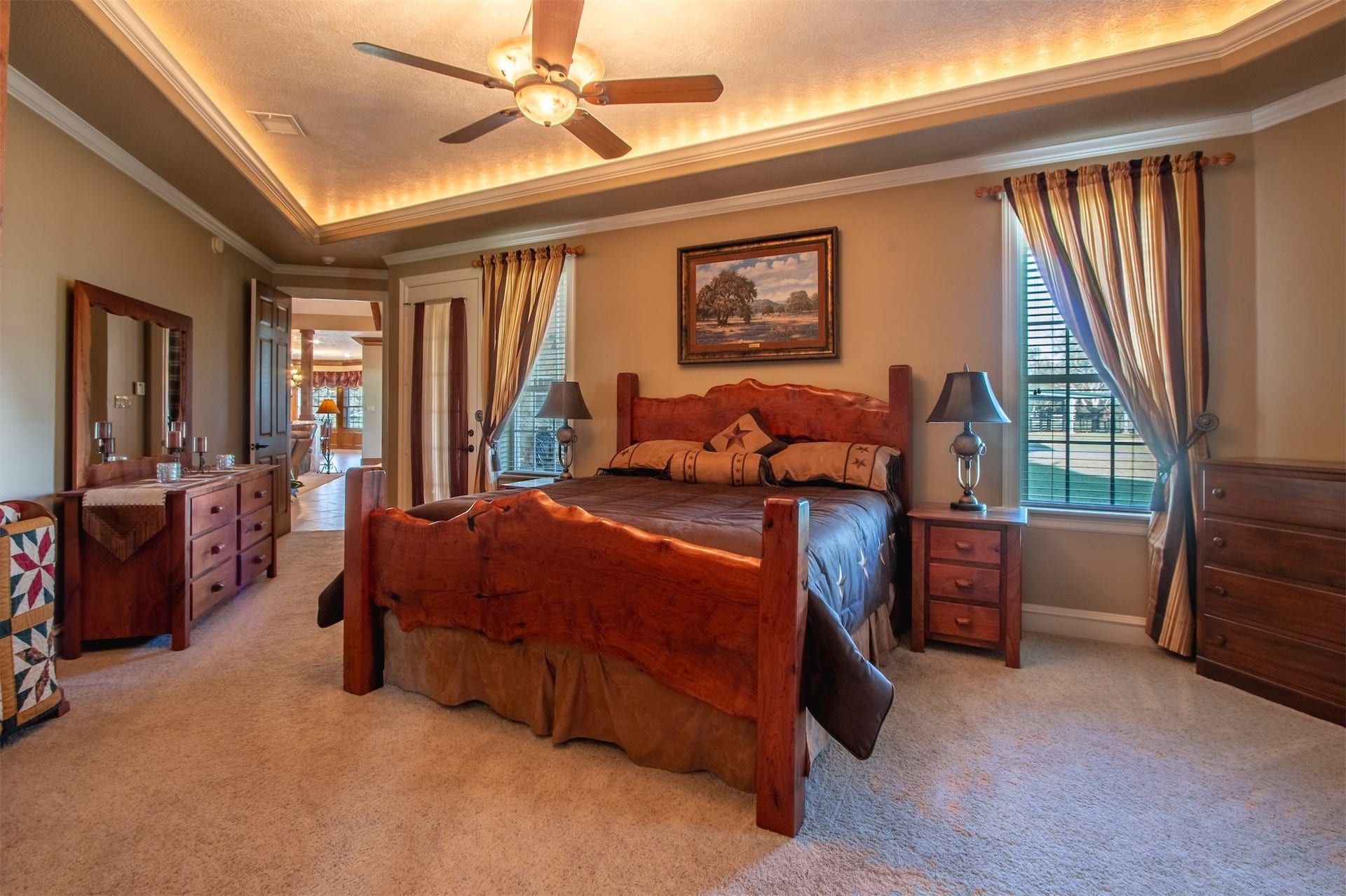 3150 Holmes Road Road, Richmond, TX 77406 Luxurious primary bedroom featuring a custom wood bed, elegant tray ceiling with ambient lighting, and large windows for natural light.