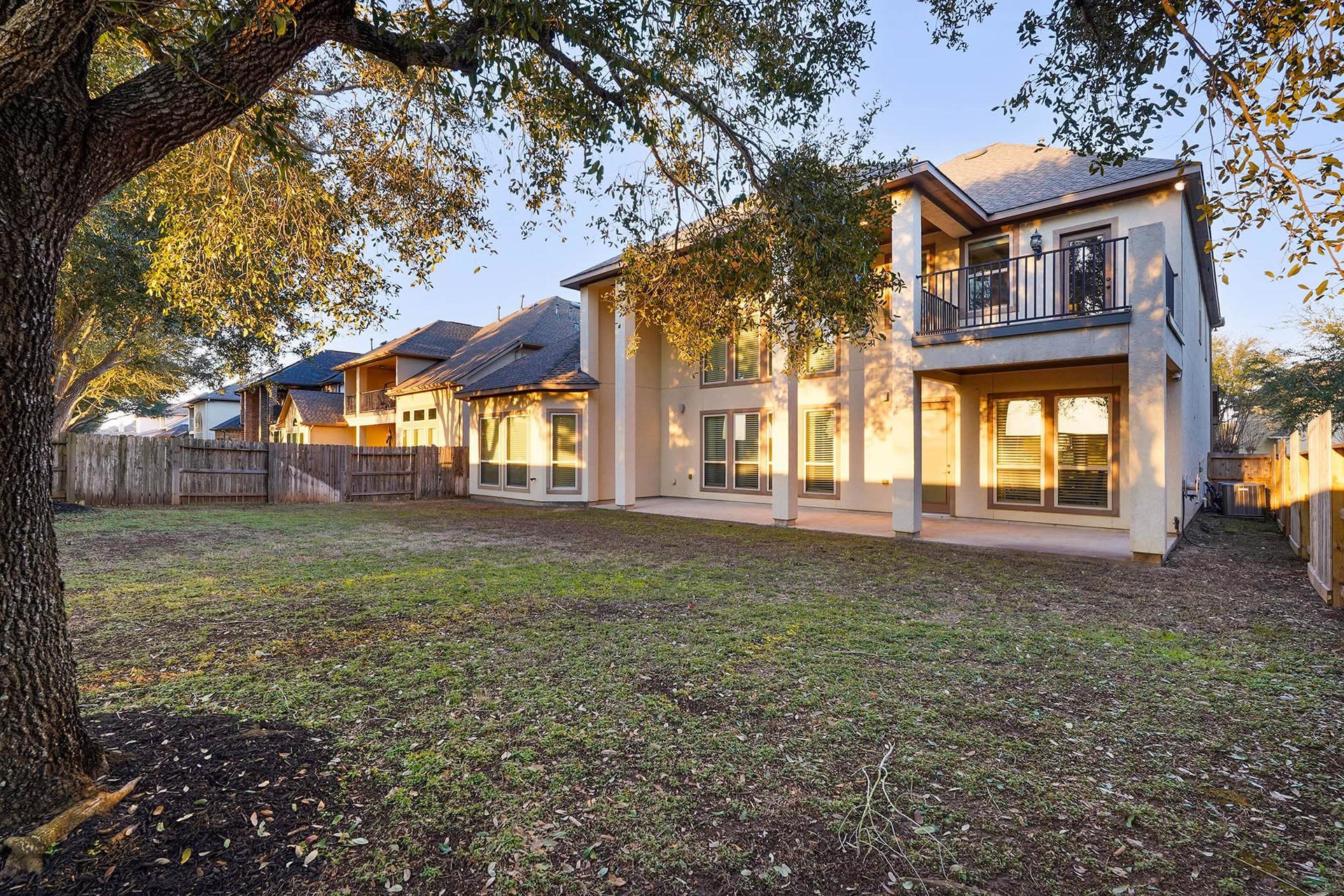 3102 Barrons Way, Sugar Land, TX 77479 This photo showcases a spacious backyard with a large two-story house. The home features numerous windows for natural light and a balcony on the second floor. The yard is partially shaded by mature trees, offering a comfortable outdoor space.