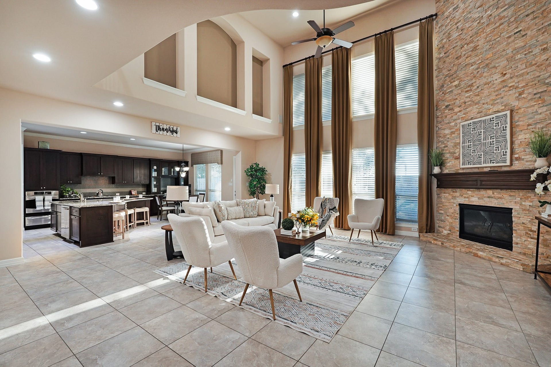 3102 Barrons Way, Sugar Land, TX 77479 The large family area features high ceilings, large windows with elegant drapes, and a cozy stone fireplace. It flows seamlessly into an open-concept kitchen with dark cabinetry and a central island, perfect for entertaining.