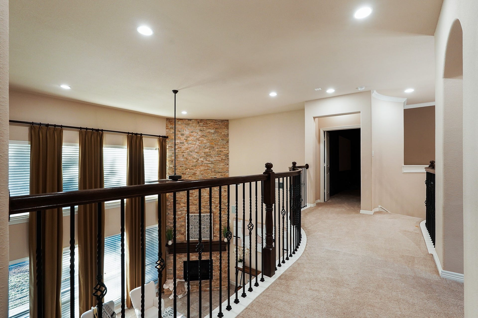3102 Barrons Way, Sugar Land, TX 77479 This photo showcases a spacious upstairs hallway featuring elegant railings overlooking a living area with high ceilings and a stone accent wall. The area is well-lit with recessed lighting and has multiple doorways leading to other rooms, offering a warm and inviting ambiance.